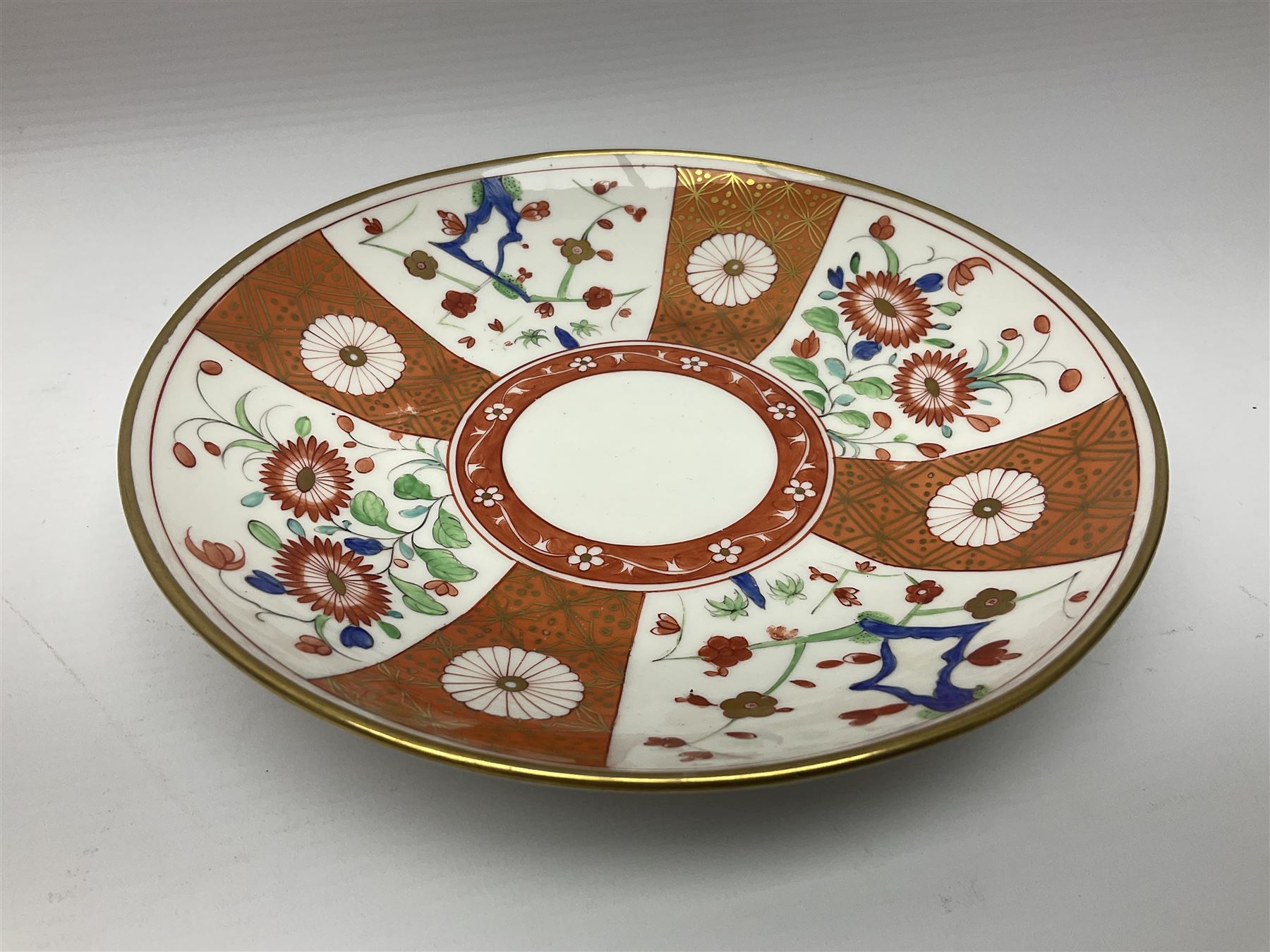 Three 18th century Worcester desert dishes, the first example decorated in the Scarlet Japan pattern, circa 1790, painted with alternating panels of Kakiemon style prunus blossom and chrysanthemum, and orange ground panels with gilt fret detail, D19cm, the second example, circa 1770, decorated with Kakiemon style chrysanthemums and foliage within shaped reserves upon a blue scale ground, with fretted square pseudo mark beneath, D19cm, and the third, circa 1770, painted with polychrome floral sprays and sprigs, D20cm