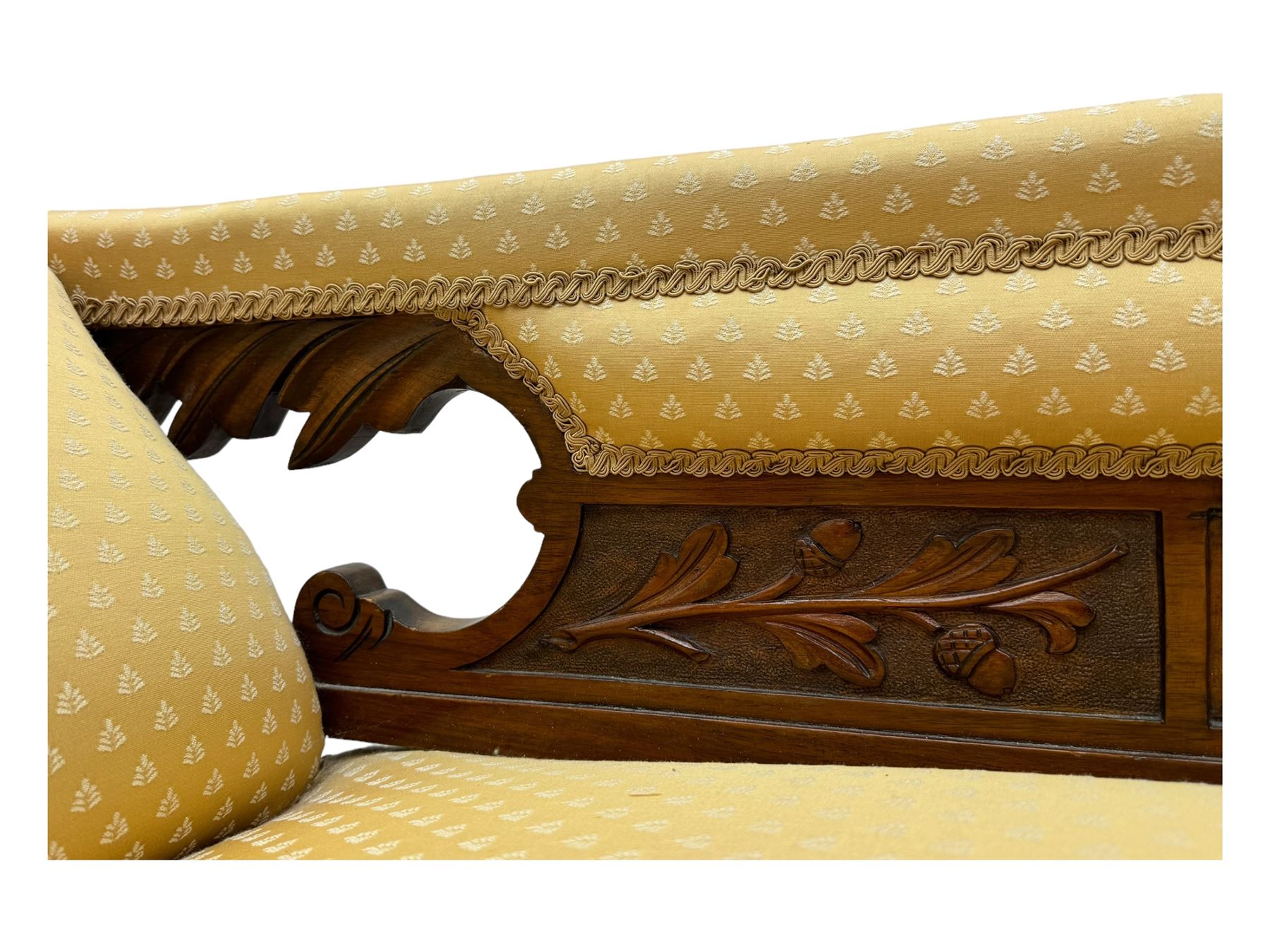 Late Victorian walnut framed chaise longue, scrolled backrest and sides upholstered in patterned yellow fabric, carved floral motifs to the backrest and sides, raised on turned supports with castors