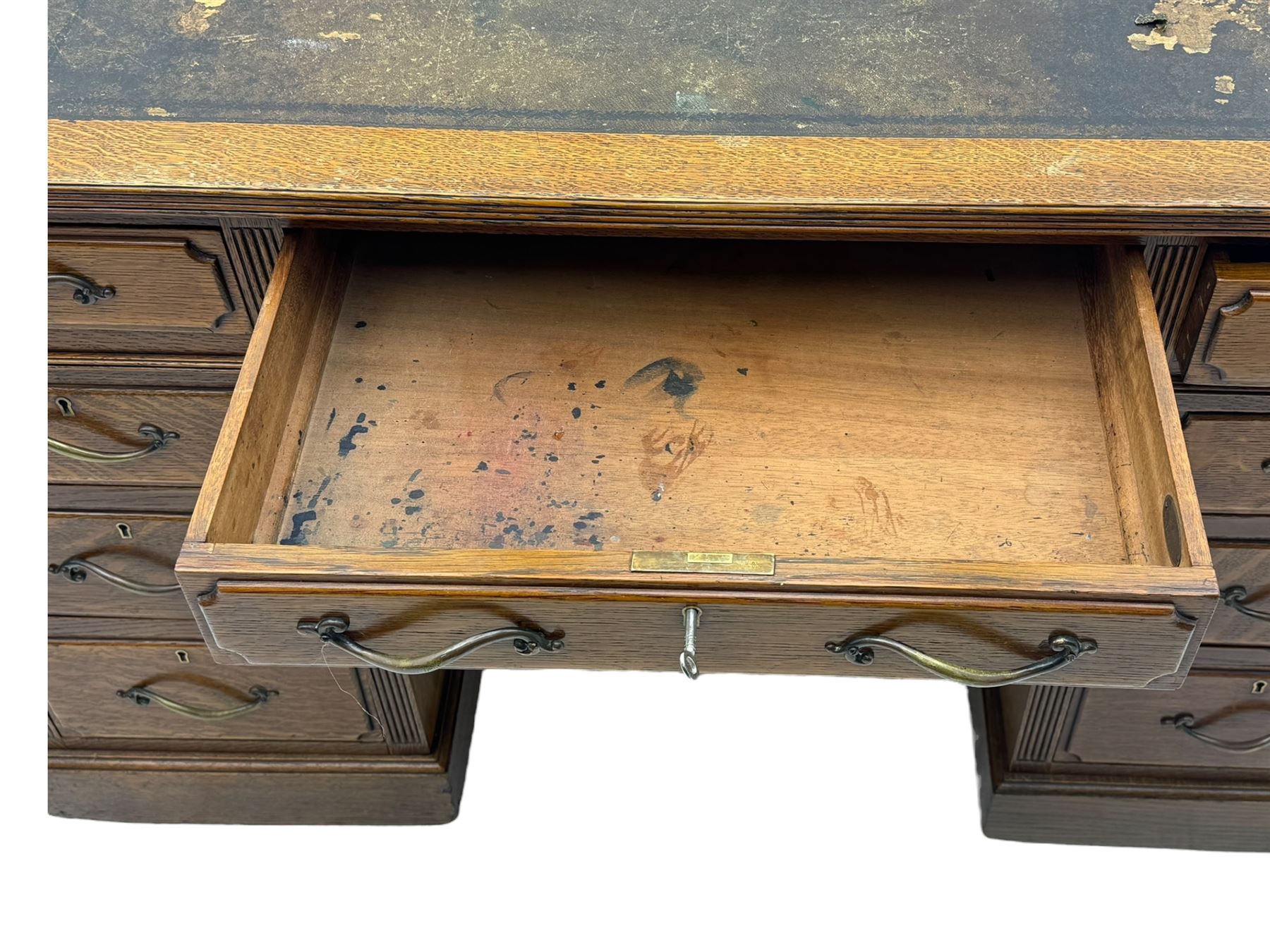 20th century oak twin pedestal desk, rectangular top with inset leather writing surface, fitted with nine drawers with chamfered edges to the raised panels, each with curved brass handles with scroll ends and keyholes, fluted detailing to the top and between the drawers, on moulded plinth base with castors