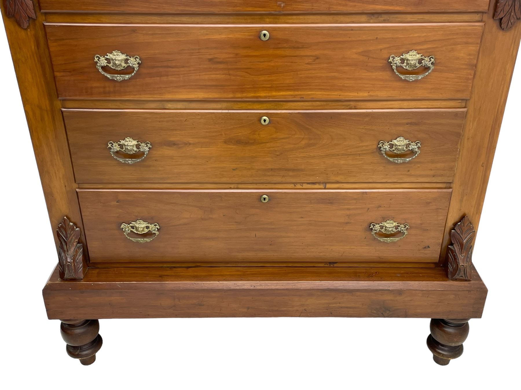 Late Victorian walnut Scotch chest, projecting cornice with turned quarter column mounts over matching half column to frieze, fitted with two upper short drawers with central cupboard, bevelled mirror glazed cupboard door, four graduating drawers below, foliage and flower head carved brackets to the uprights, panelled sides, chamfered plinth on turned feet