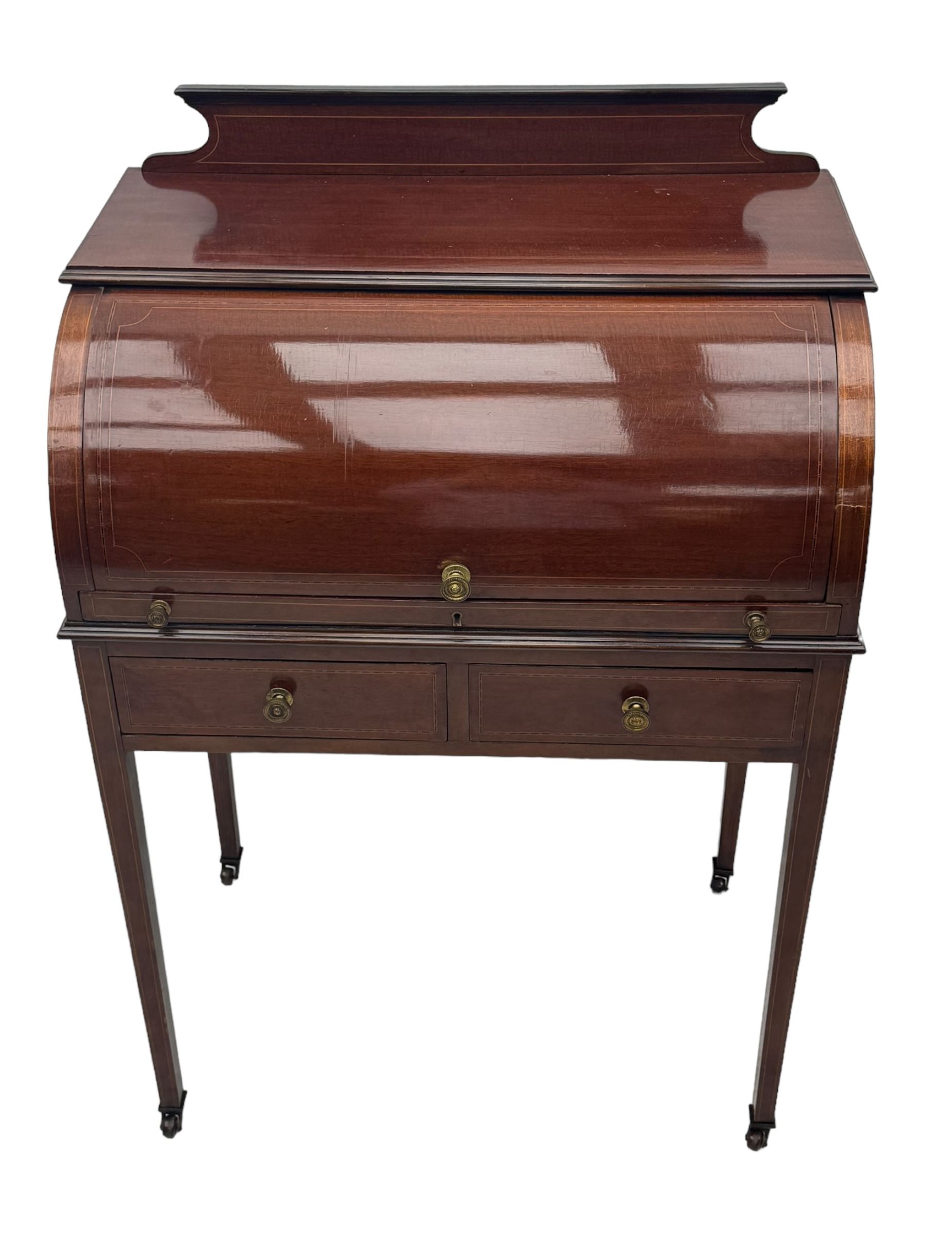 Edwardian inlaid mahogany roll-top desk, cylindrical lid enclosing fitted interior with pigeonholes, drawers and retractable writing surface, over two drawers with brass pull handles, on tapered supports with brass and ceramic castors