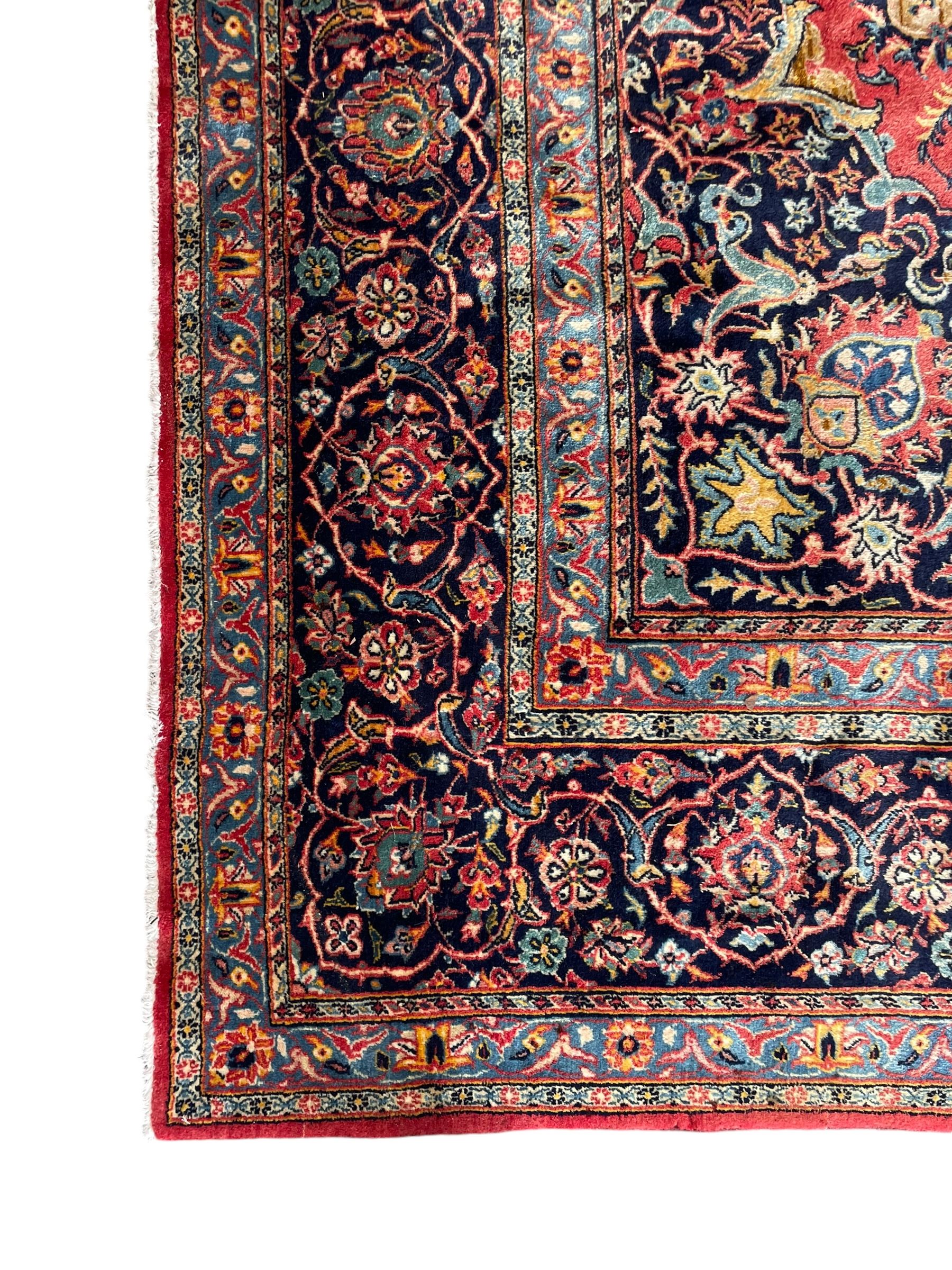 Persian Kashan crimson ground carpet, central rosette medallion on a field of trailing foliate branches decorated with palmettes, scrolling border with repeating plant motifs and flower heads, enclosed within floral pattern guard stripes