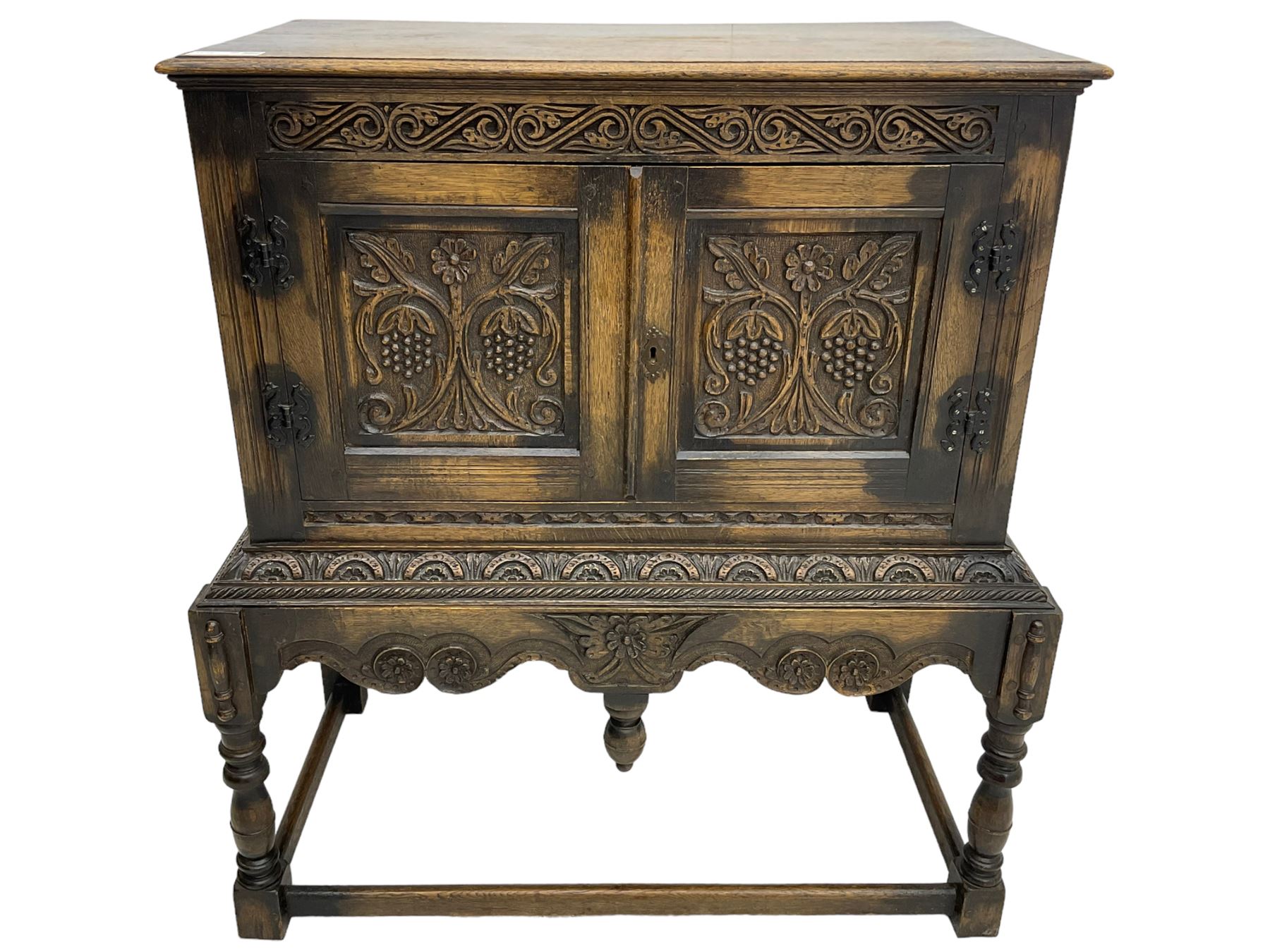 Jacobean Revival carved oak cupboard, moulded rectangular top over S-scroll carved frieze and two doors, the panelled doors carved with stylised plant motifs, on stand decorated with lunettes and shaped apron with hanging turned pendant, on turned supports united by stretchers 