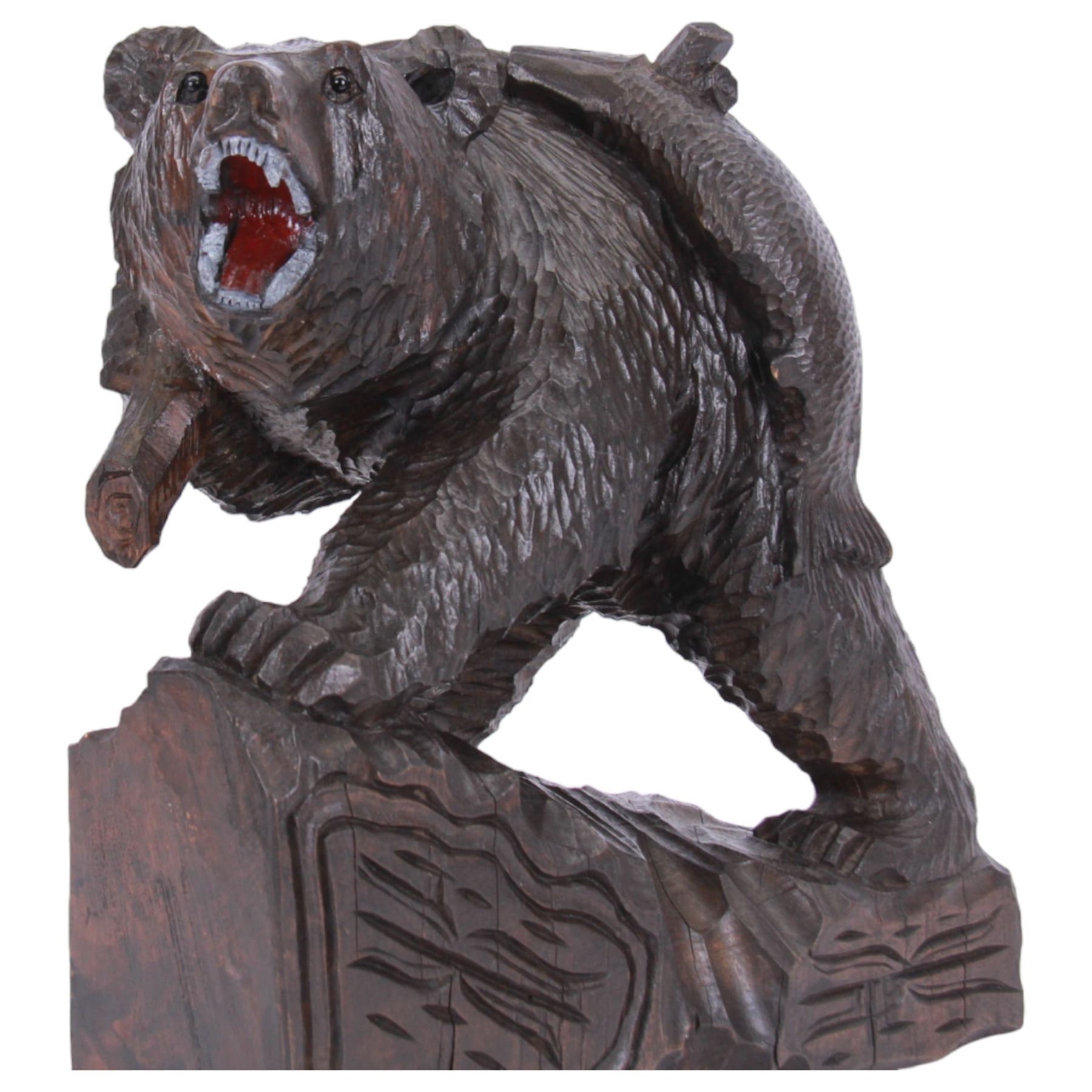 20th century Black Forest carving of a bear carrying a fish upon its back, with open mouth, painted tongue and teeth, and inset glass eyes, stood  upon a naturalistic base, overall H37cm L34cm W18cm