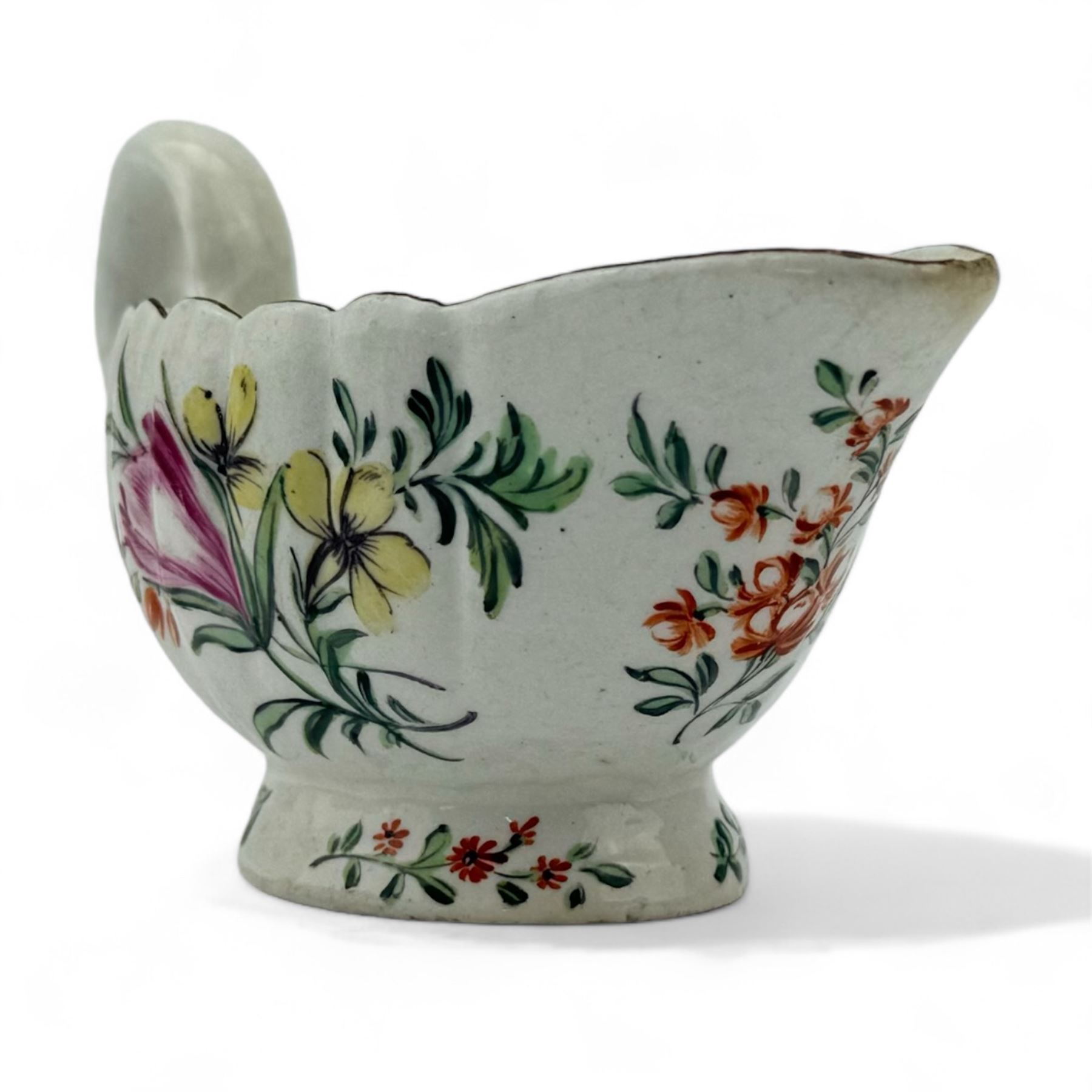 18th century butter boat, the fluted body and pedestal foot hand painted in polychrome enamels with floral bouquets and sprigs within a brown painted rim, possibly Bow, L13cm