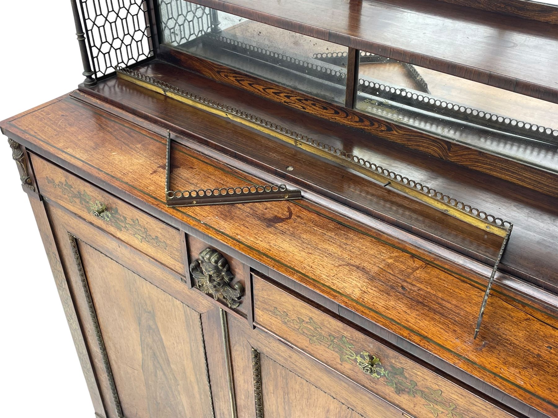 Attributed to John McLean & Son (London: 1770-1825) - Regency rosewood chiffonier, the raised two tier mirrored back on turned brass supports with brass trestle sides, rectangular top with brass stringing over two drawers and central cast brass satyr mask, cock-beaded drawer fronts inlaid with extending stylised foliate brass work, double cupboard below enclosed by panelled doors with cast egg and dart edging, matched brass inlays to the uprights, fitted with internal shelf, on turned compressed bun feet 