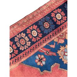 Afghan rust ground carpet, large central lozenge medallion decorated with stylised plant motifs, running water guard stripes enclosing indigo ground border decorated with stylised flower heads