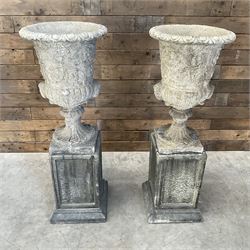 Pair of Georgian design cast stone garden urns, egg and dart rim with raised floral motifs, pedestal base terminating on square plinth, raised on square block plinth