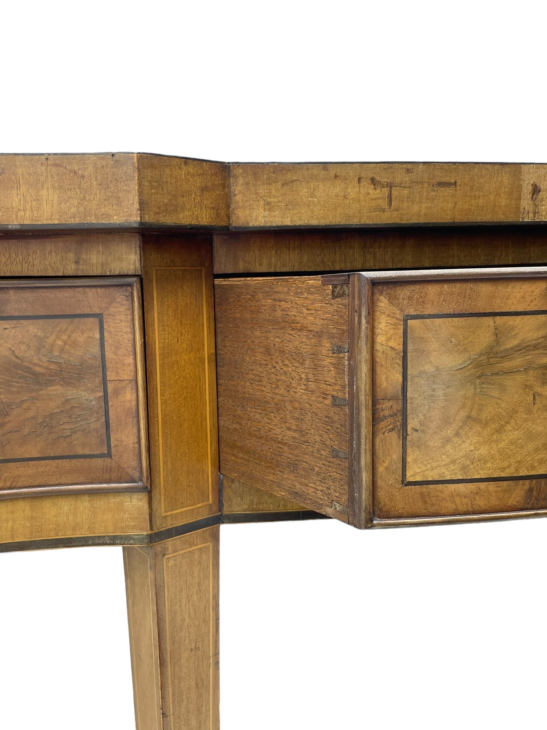 Large George III mahogany serpentine serving table, shaped top with crossing banding and stringing, the frieze fitted with three cock-beaded drawers, oval pressed brass handle plates decorated with urns, on square tapering supports with spade feet 