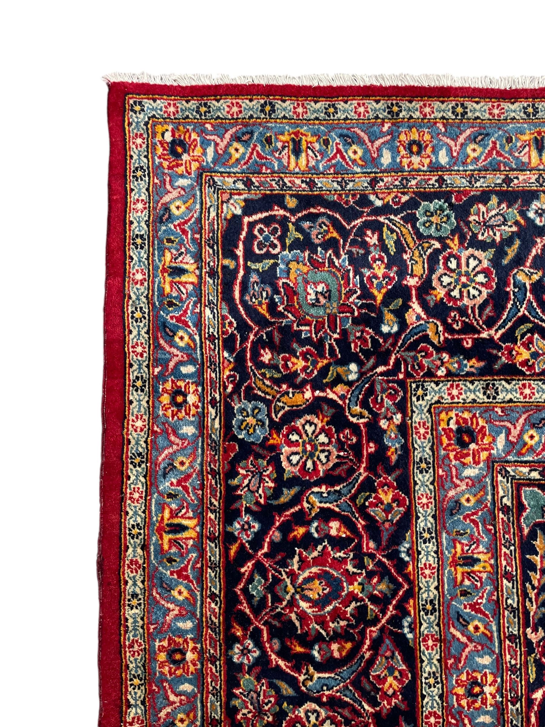 Persian Kashan crimson ground carpet, central rosette medallion on a field of trailing foliate branches decorated with palmettes, scrolling border with repeating plant motifs and flower heads, enclosed within floral pattern guard stripes