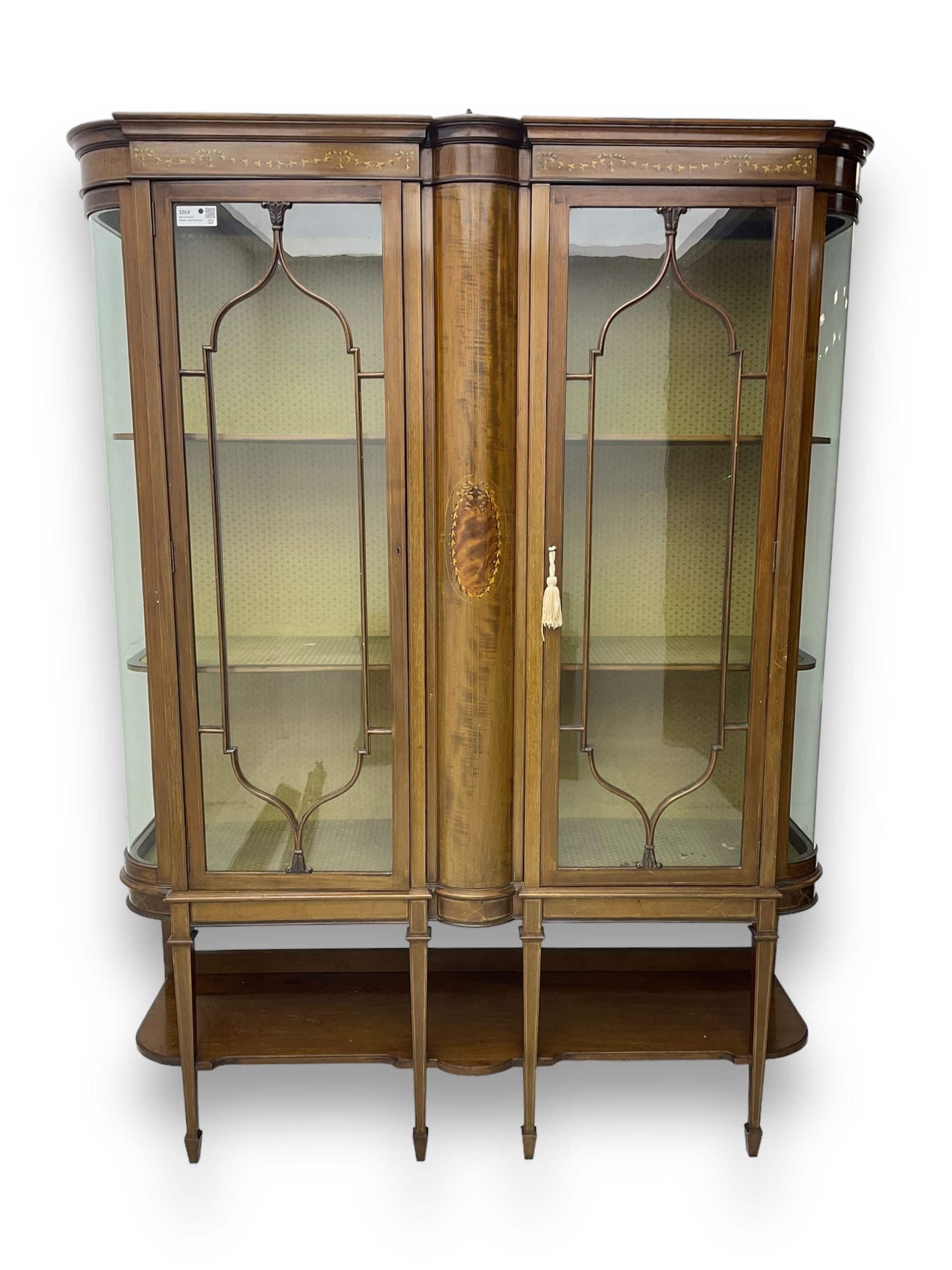 Edwardian inlaid mahogany display cabinet, projecting moulded cornice over two glazed doors, flanked by curved glazed sides and central arched panel with floral medallion, raised on square tapering supports with spade feet united by undertier