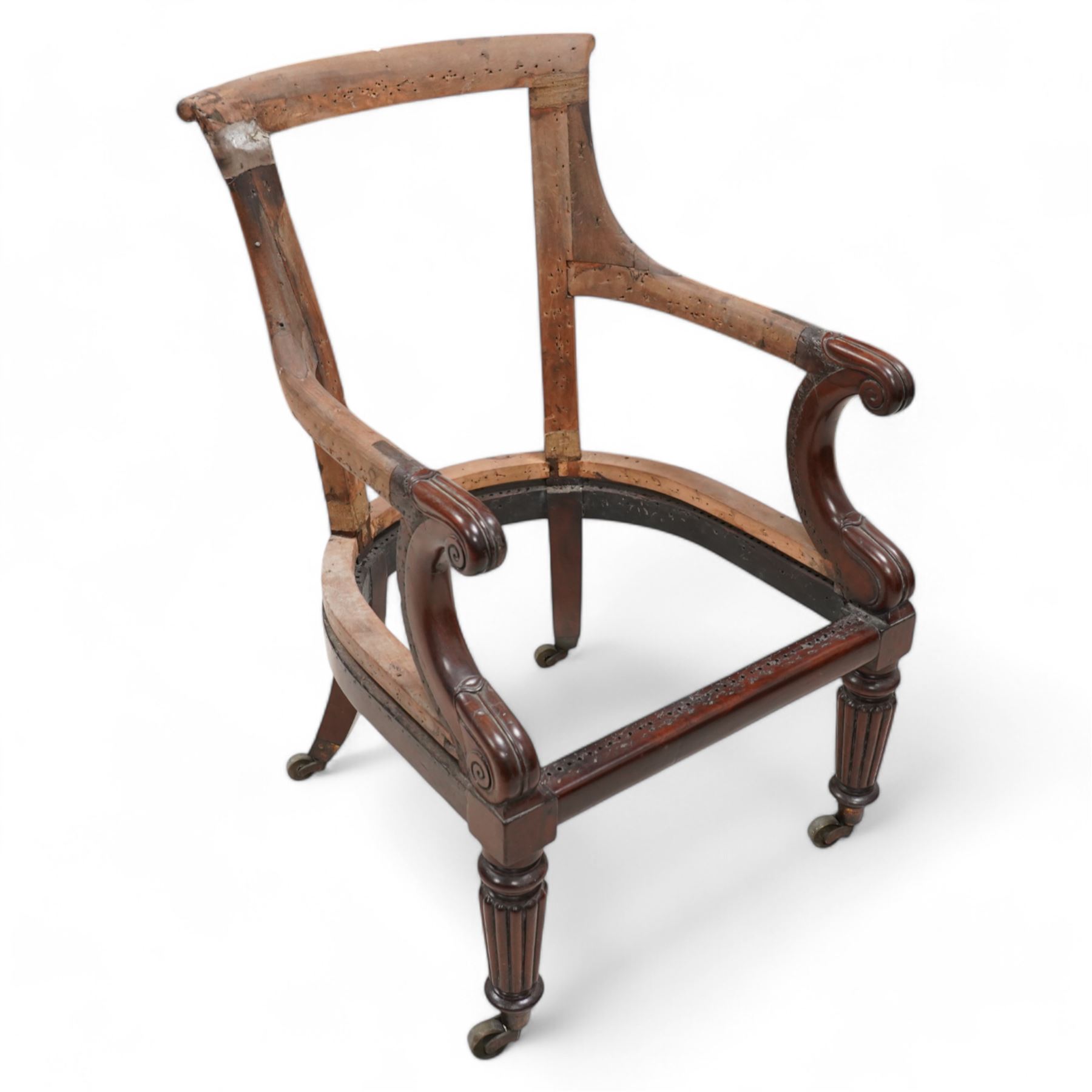 Regency mahogany and hardwood-framed library chair, curved and rolled cresting rail over scroll and lappet carved arm terminals, on turned and reed carved supports with brass castors 