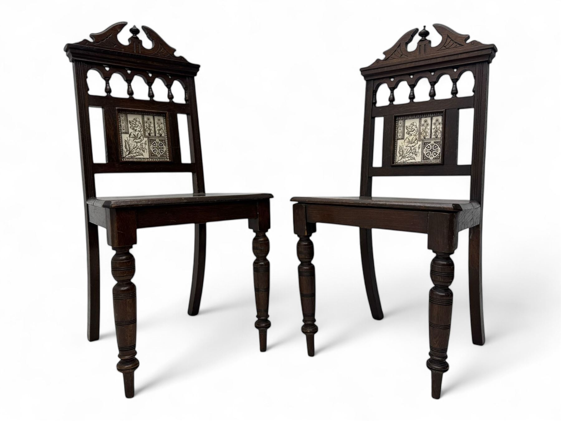 Pair of late Victorian oak hall chairs, shaped pediment over spindle turnings and tiled back, on ring turned supports 