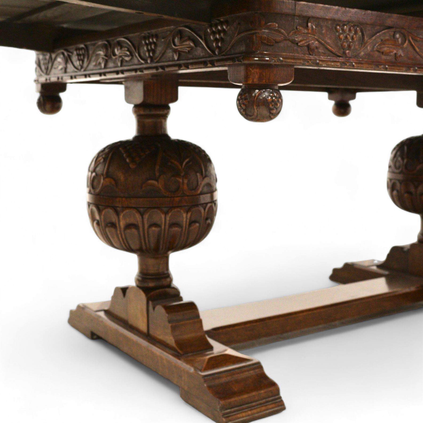 Early 20th century heavily carved oak draw leaf dining table, shaped rectangular top with recessed bead moulded edge, grape-vine carved frieze over large baluster vine and lobe carved end supports on sledge feet united by stretcher; with matched set of six dining chairs, upholstered in coral pink fabric 