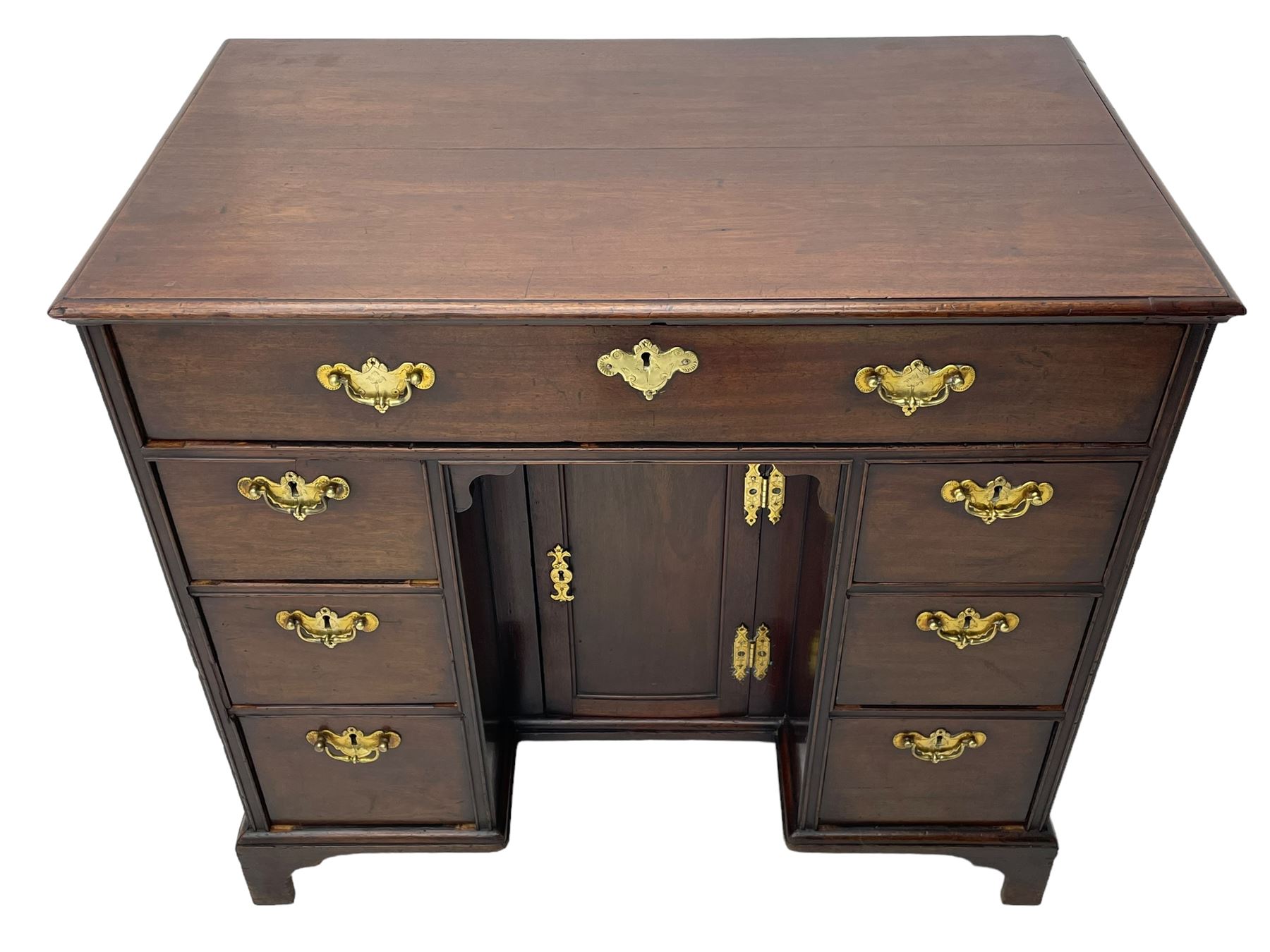 George III mahogany kneehole desk, moulded rectangular top over one long drawer, six short drawers and recessed panelled cupboard, cock-bead moulded frame, fitted with shaped brass handle plates with engraved decoration, on bracket feet 