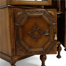 Early 20th century heavily carved oak display cabinet, frieze carved with grape vines over three astragal glazed doors with bevelled glass, over three cupboards applied with octagonal carved panels with further vine carvings, on turned and lobe carved supports