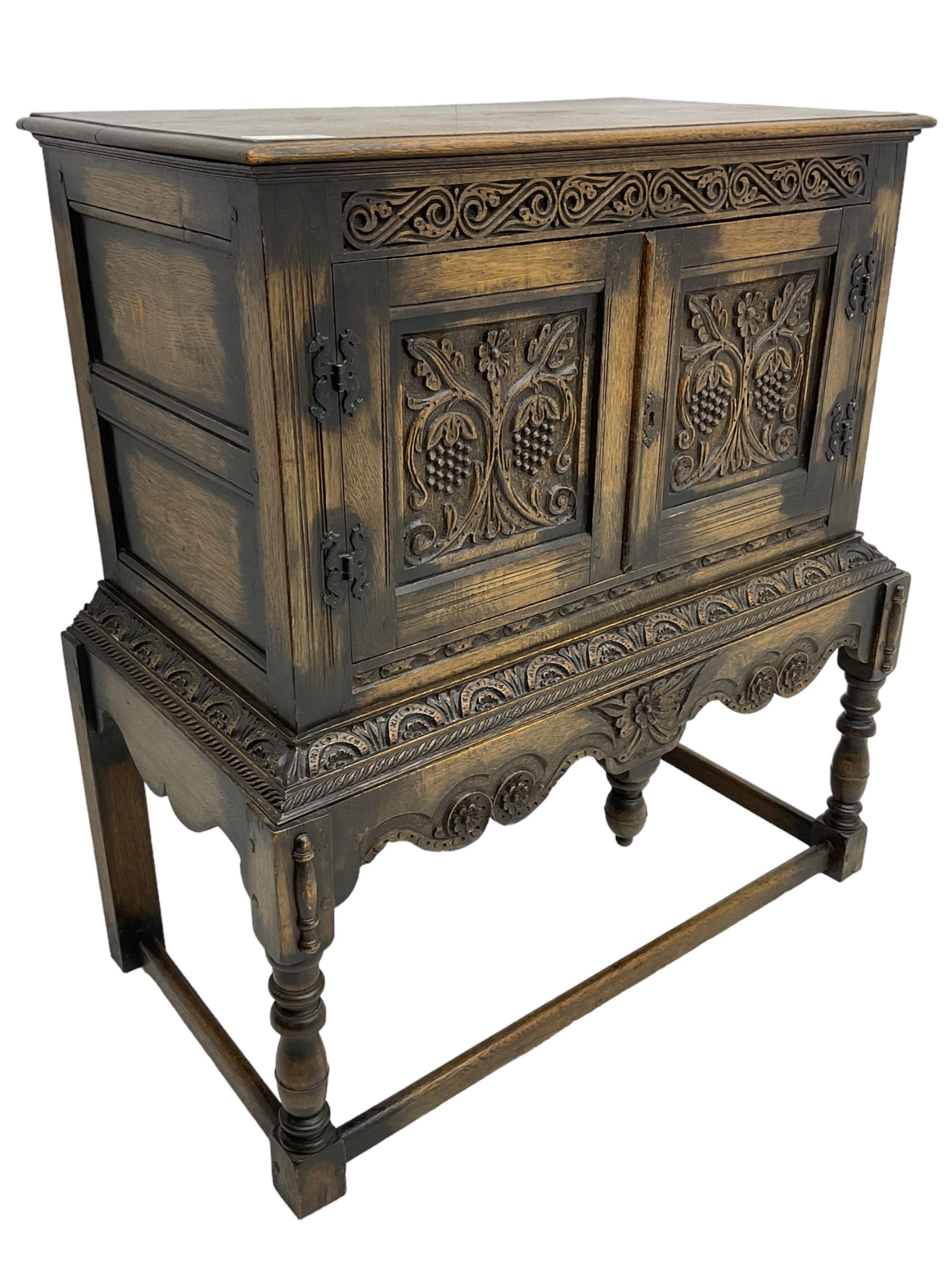 Jacobean Revival carved oak cupboard, moulded rectangular top over S-scroll carved frieze and two doors, the panelled doors carved with stylised plant motifs, on stand decorated with lunettes and shaped apron with hanging turned pendant, on turned supports united by stretchers 