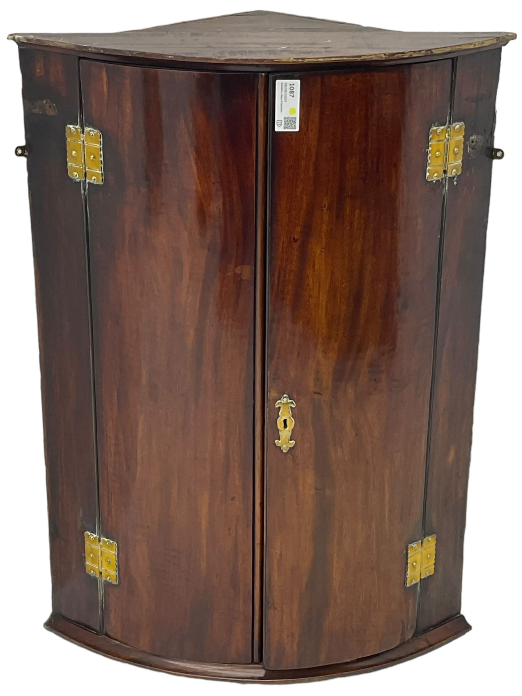 George III mahogany bow-front corner cupboard, enclosed by two figured doors with brass hinges and escutcheon, the painted interior fitted with three shelves 