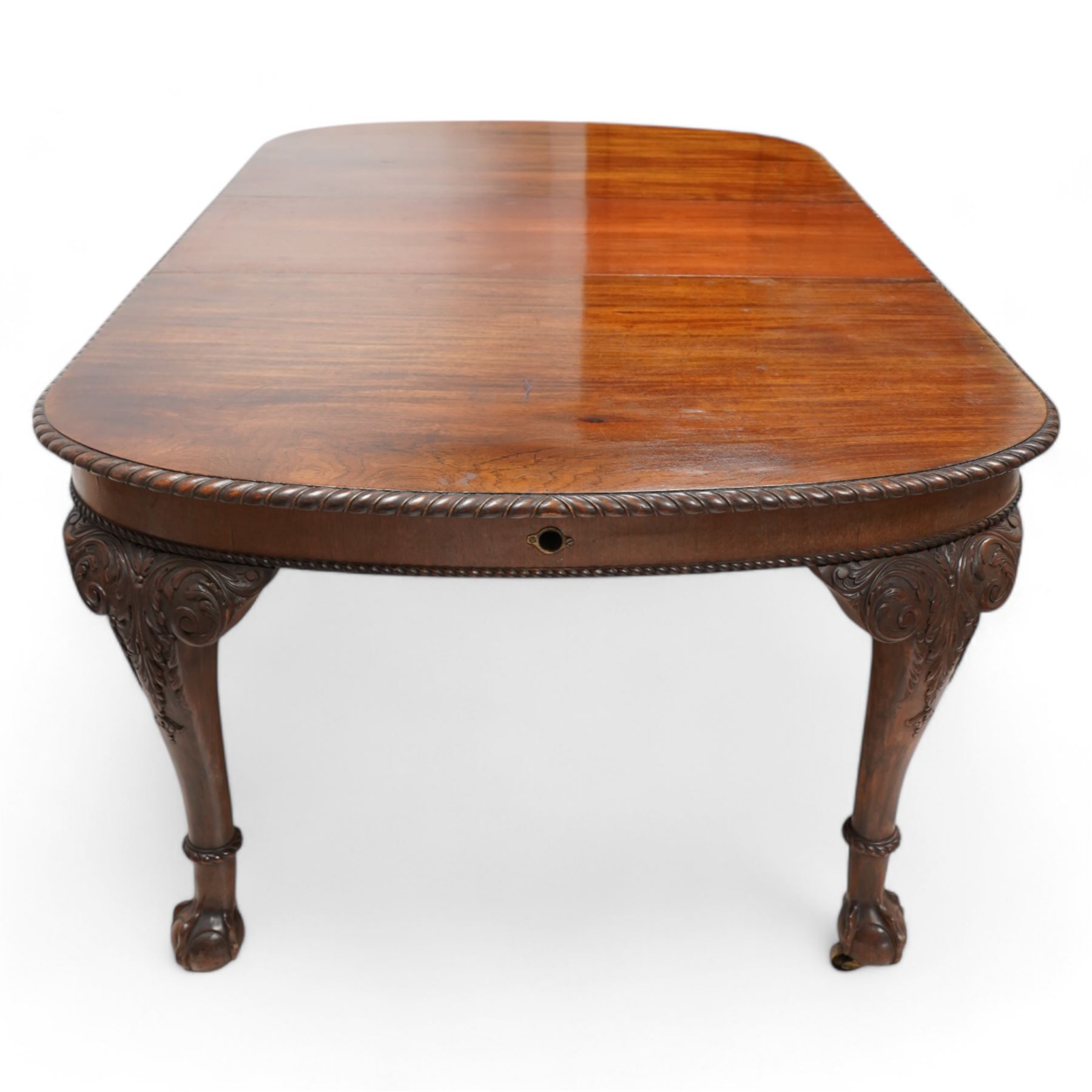 Early 20th century telescopic extending dining table, gardroon carved rectangular top with rounded ends, scrolled acanthus leaf carved cabriole supports with ball and claw feet, on brass castors, with two additional leaves  