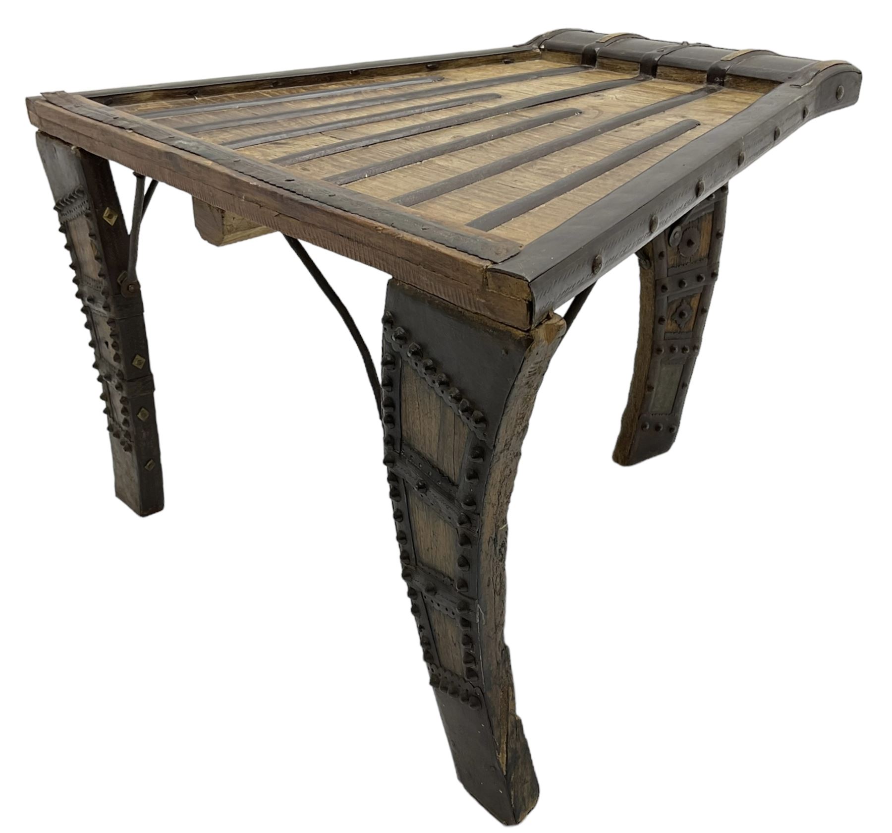 19th century Indian bullock / ox cart converted coffee table, trapezoidal top with applied metal decoration and iron stretchers, raised on three swept supports with stud decoration