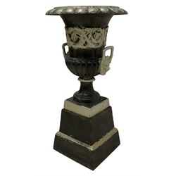 20th century cast iron Campana-shaped urn on plinth, with scrolling foliate relief decoration, in ebonised and silver painted finish