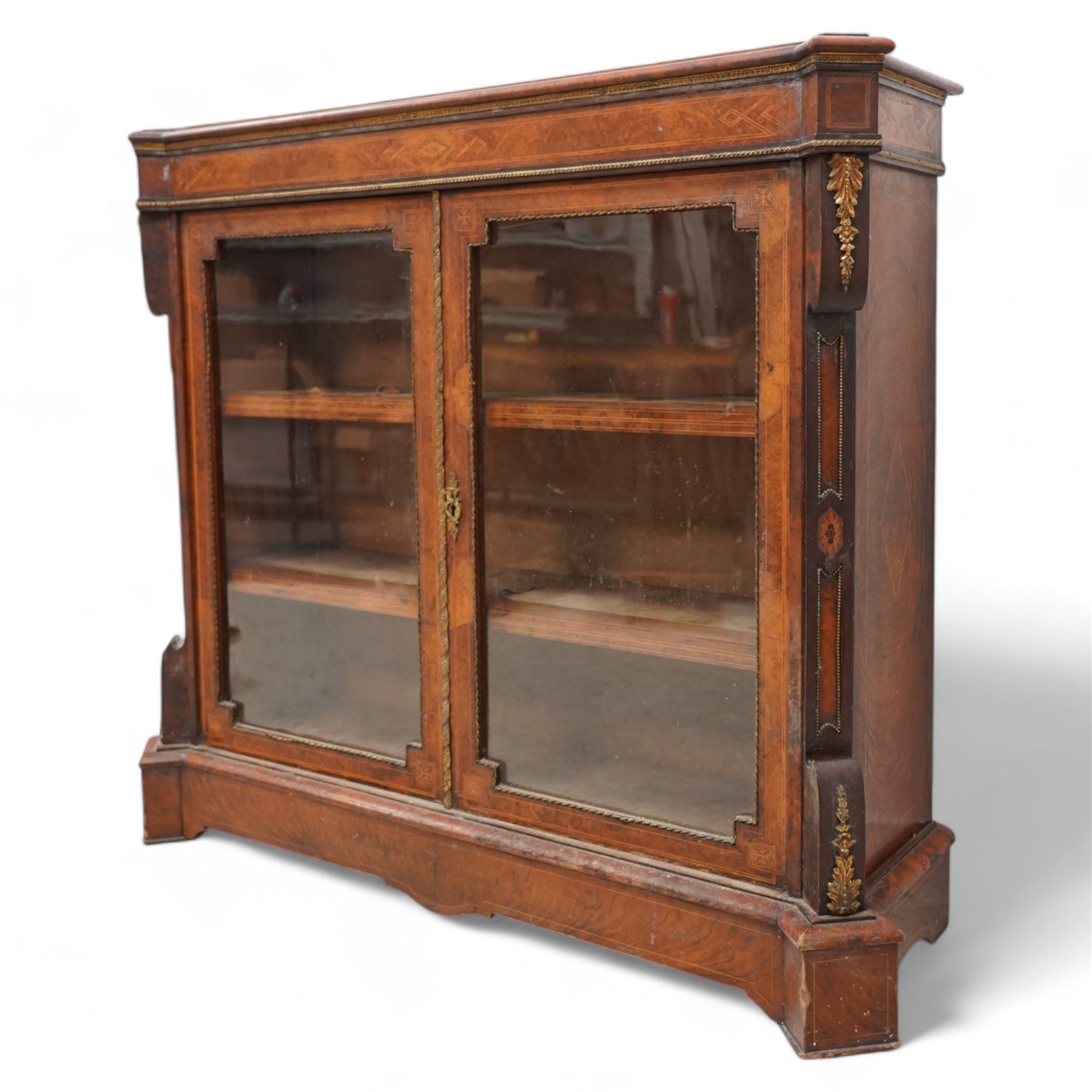 Victorian inlaid walnut and gilt metal mounted pier display cabinet, moulded rectangular top with extending square corners, the frieze inlaid with geometric satinwood bands and decorated with gilt metal edging, two glazed doors enclosing two shelves, enclosed by canted corners with recessed panels and gilt metal mounts, on moulded skirt base 