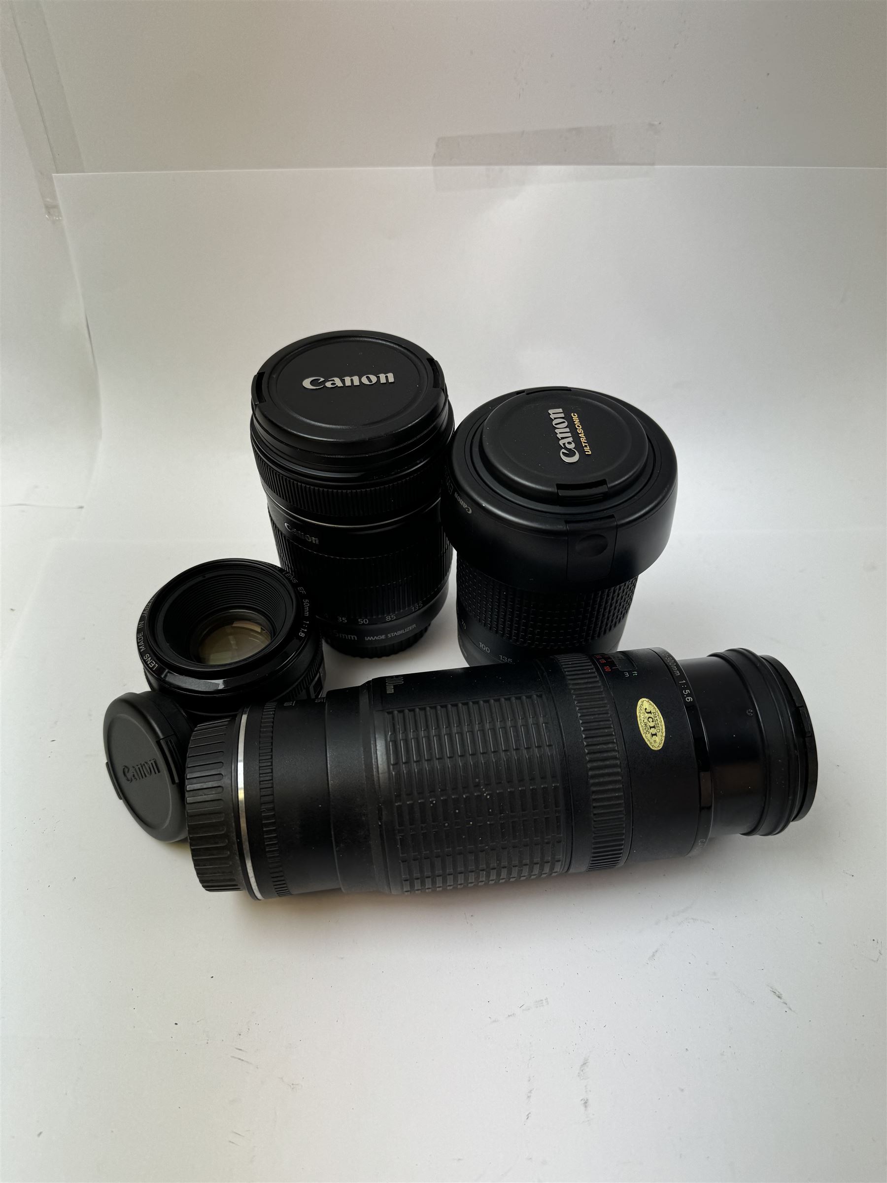 Three Canon EF camera lenses, comprising 100-300mm 1:5.6 lens serial no. 1057918, 50mm 1-1.8 lens serial no. 1153183 and a 55-200mm 1:4.5-5.6 USM zoom lens serial no. 2100282B, together with a Canon EF-S 18-135mm 1:3.5-5.6 image stabiliser lens serial no. 7242517341