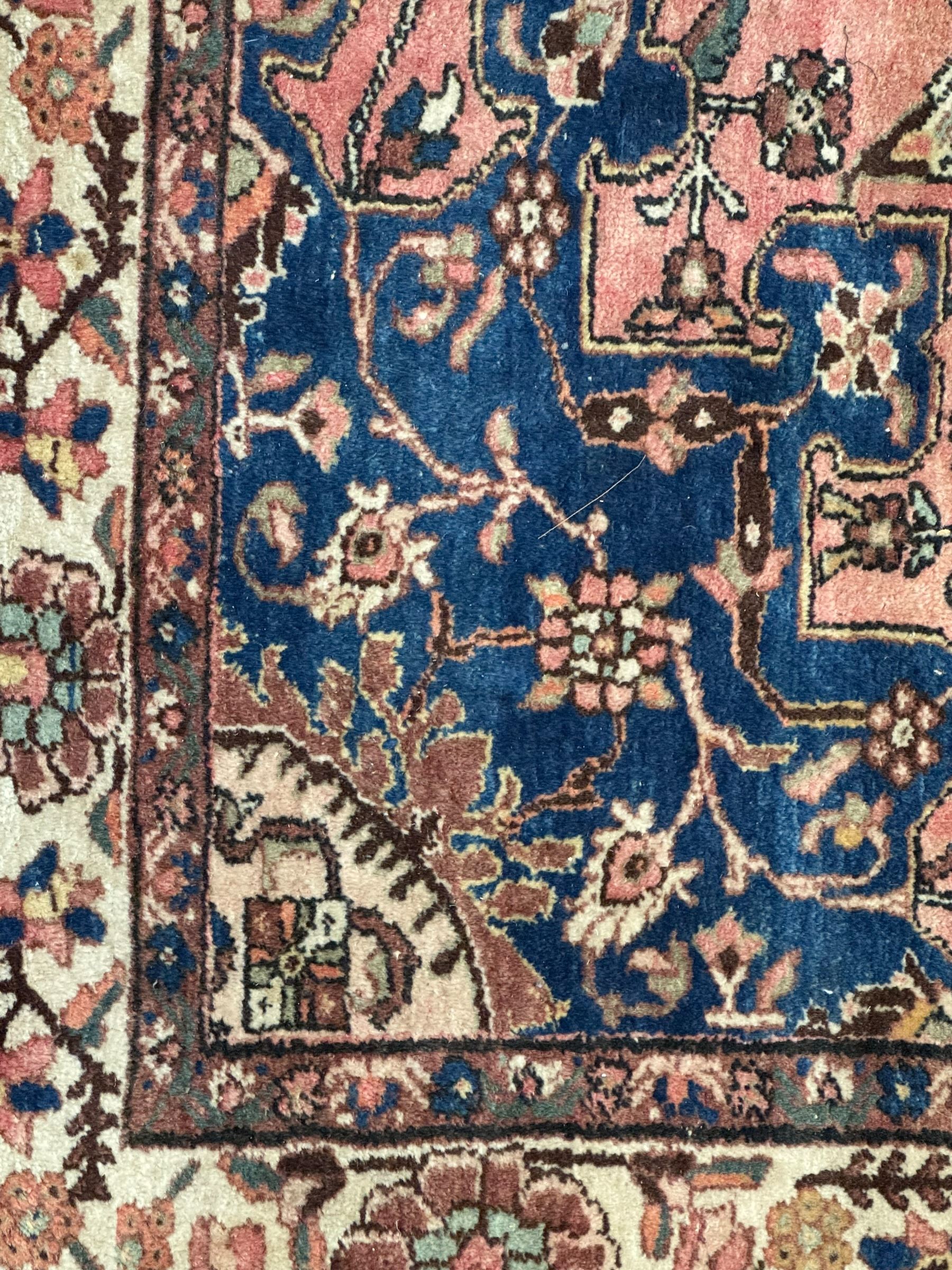 Persian Hamadan ground rug, central medallion design with a salmon pink field, accentuated by navy blue spandrels, surrounded by a stylised floral border in cream and blue tones