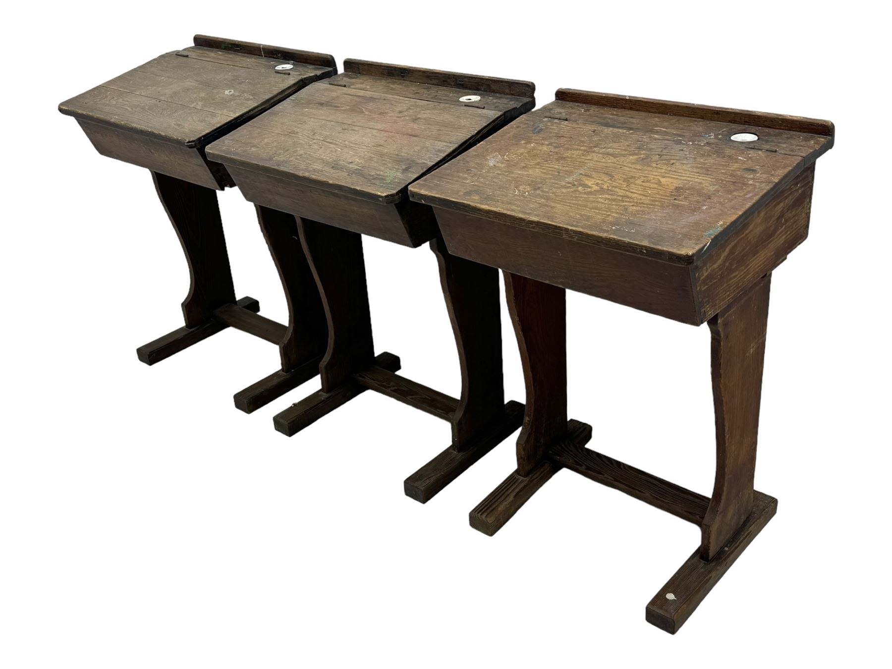 Three pitch pine school desks, each with rectangular lift-top with recessed ink well enclosing storage compartment, on trestle supports joined by stretcher