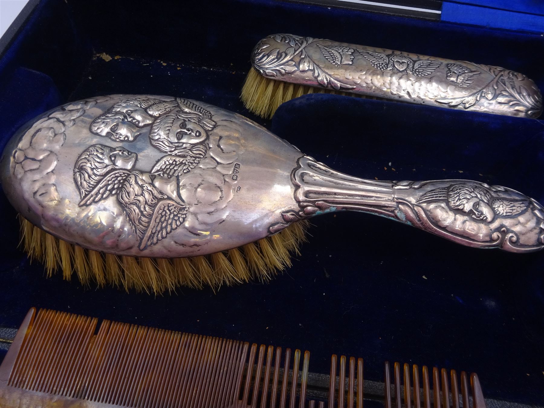 Four piece Edwardian silver mounted dressing table set, comprising hair brush, hand mirror, shoe horn and clothes brush, each embossed with cherubs, hallmarked Chester 1908, makers mark indistinct, together with a silver comb holder, hallmarked, contained within tooled leath, silk and velvet lined fitted case, 