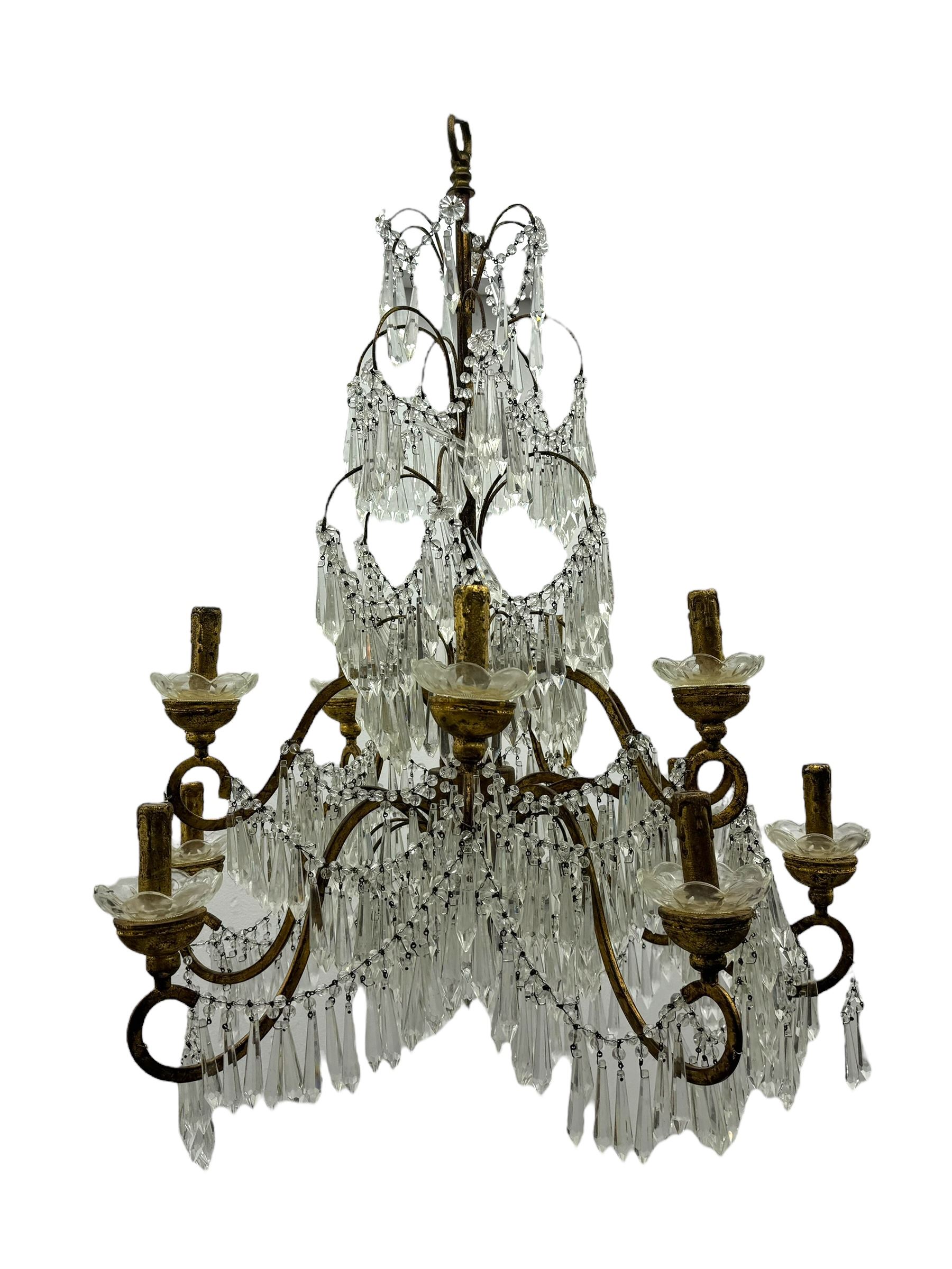 India Jane Interiors - pair of contemporary gilt bronze and crystal chandeliers, the framework featuring scrolling arms and garlands of crystal beads, each with twelve candle-style light fixtures with scalloped glass bobeches, adorned with multiple tiers of cut glass prisms, terminating in a central finial with a suspension loop