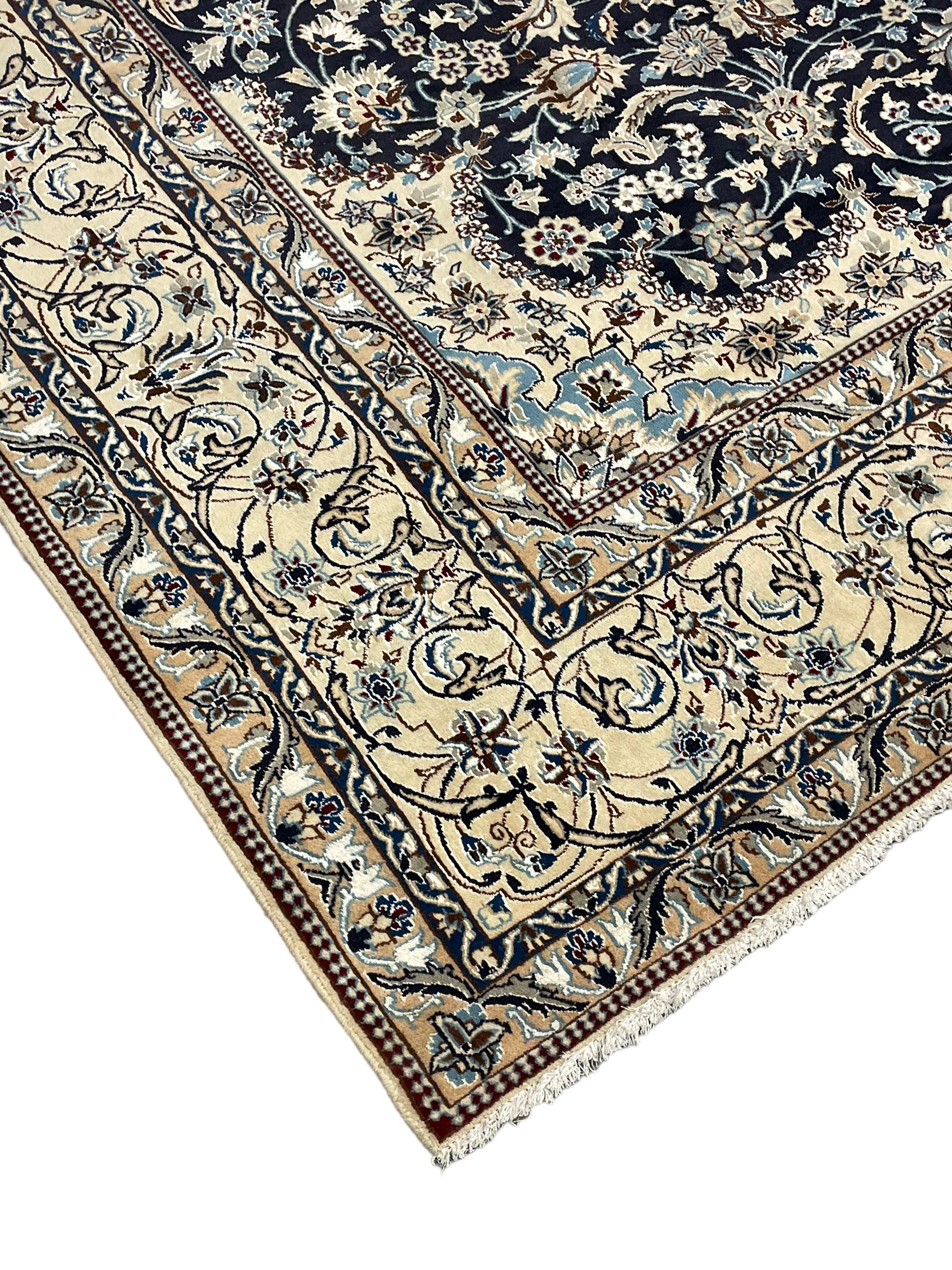 Persian Kashan indigo ground carpet, the central ivory rosette medallion surrounded by trailing and interlaced flower heads and branches, matching spandrels with floral design, the border with scrolling pattern decorated with stylised plant motifs within guards