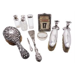 Group of silver, comprising Victorian silver mounted perpetual calendar with various date cards, hallmarked Henry Matthews, Birmingham 1900, silver mounted dressing table items, to include hair brush, with embossed decoration, pair of clothes brushes, and a shoe horn, together with a pair of silver mounted dwarf candlesticks, four cut glass jars/scent bottles with silver covers and a cut glass open salt with silver collar, all hallmarked 