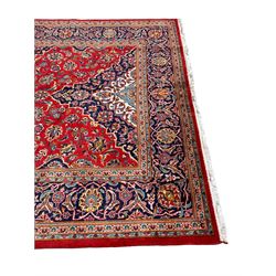 Persian Kashan crimson ground rug, overall arabesque design, the field decorated with swirled leafy branches and palmettes, indigo ground border decorated with repeating pattern, within guard stripes 