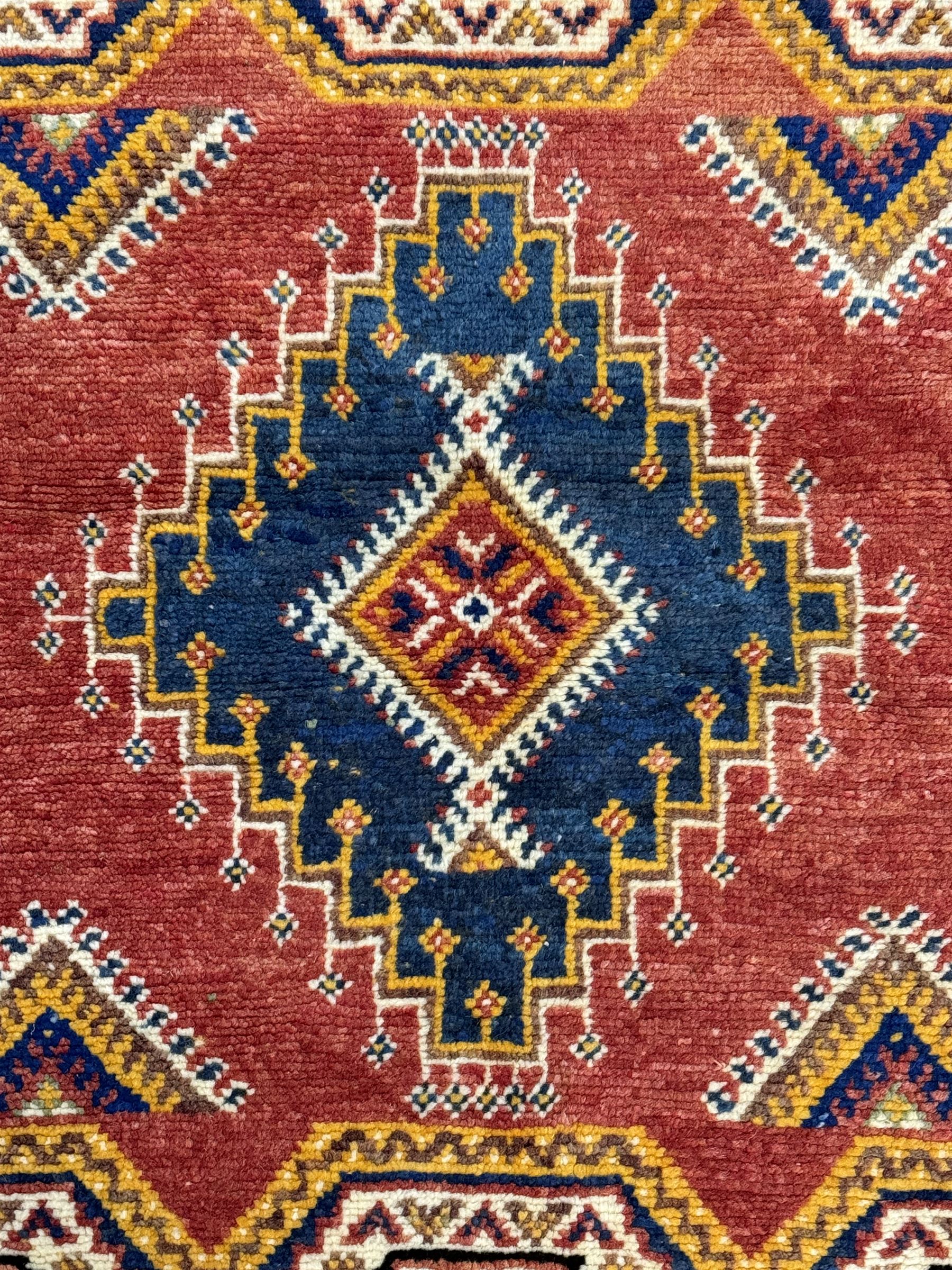 Persian Qashqai crimson ground rug, the field with central indigo and yellow medallion with geometric motifs, flanked by smaller medallions, border with repeating patterns (112cm x 200cm); Turkish Kazak light blue ground rug (109cm x 193cm); red ground runner with three octagonal medallions (69cm x 138cm)