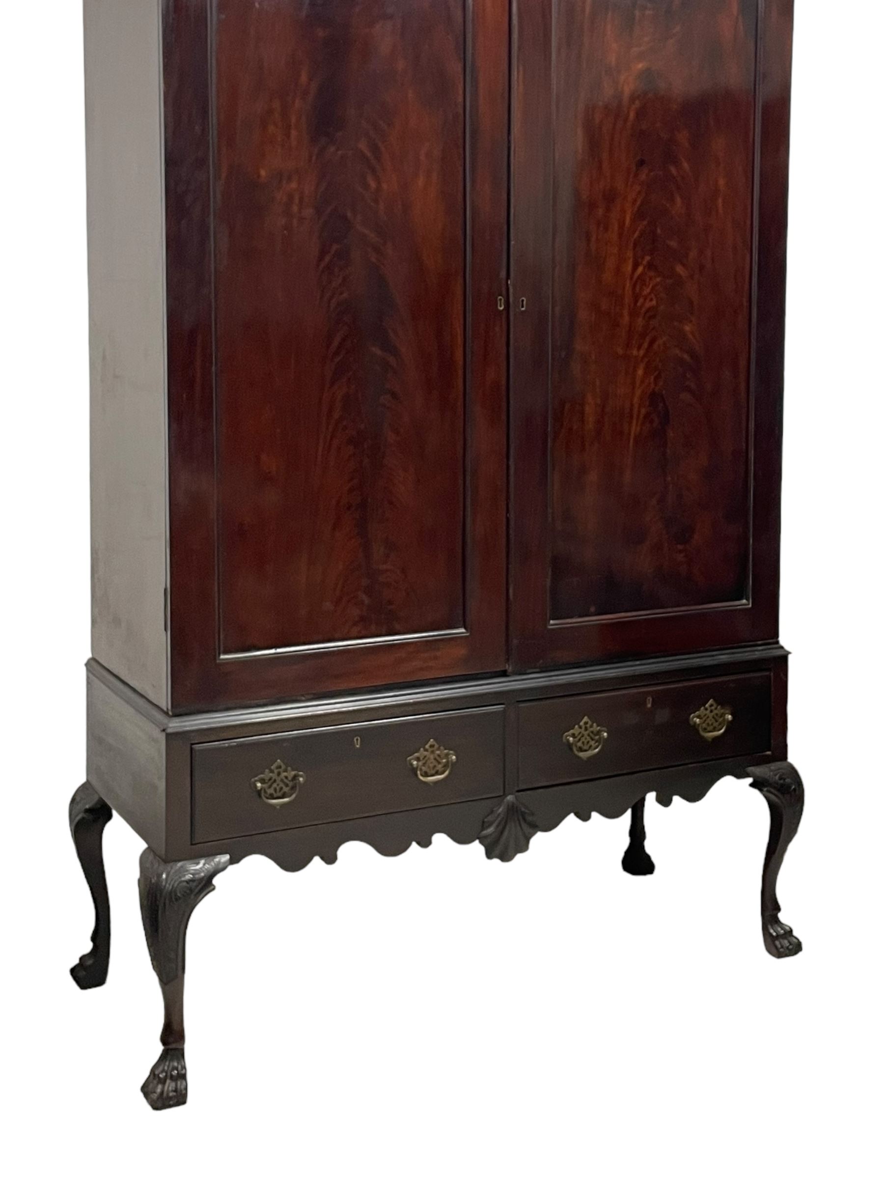 19th century Irish mahogany press wardrobe, projecting dentil cornice over two figured panelled doors, enclosing three sliding trays and hanging rail with coat hooks, fitted with two drawers to base over a shaped apron, raised on acanthus carved cabriole supports with paw feet, retailed by Millar & Beatty of Dublin, with paper labels verso, collected and restored by Michael Butler (1870-1900), impressed stamp to side and ink stamp to drawer inscribed 'M Butler collector of high-class furniture and works of art'