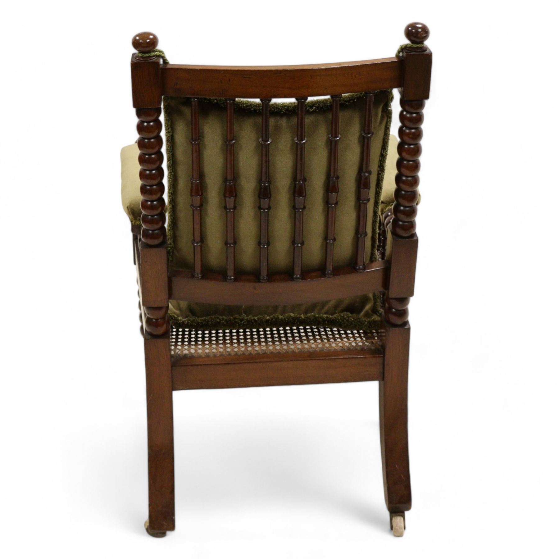 Late Victorian walnut bobbin turned armchair, curved cresting rail with bead moulding over turned spindle back, upholstered arms on turned balustrade supports, cane work seat over seat rail with matching bead moulding, loose seat cushion upholstered in olive green fabric, on tapering bobbin turned front supports with brass and ceramic castors, 