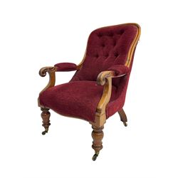 Victorian mahogany framed open armchair, upholstered in buttoned red fabric, the arm terminals carved with scrolls, on turned front supports with brass cups and castors