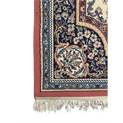 Persian design ivory ground rug, the field decorated with an oval medallion filled with floral motifs and scrolling vines, flanked by floral sprays and corner spandrels with palmette designs, the main border featuring a series of stylised floral patterns against a dark blue ground, enclosed by multiple guard stripes with geometric and floral motifs