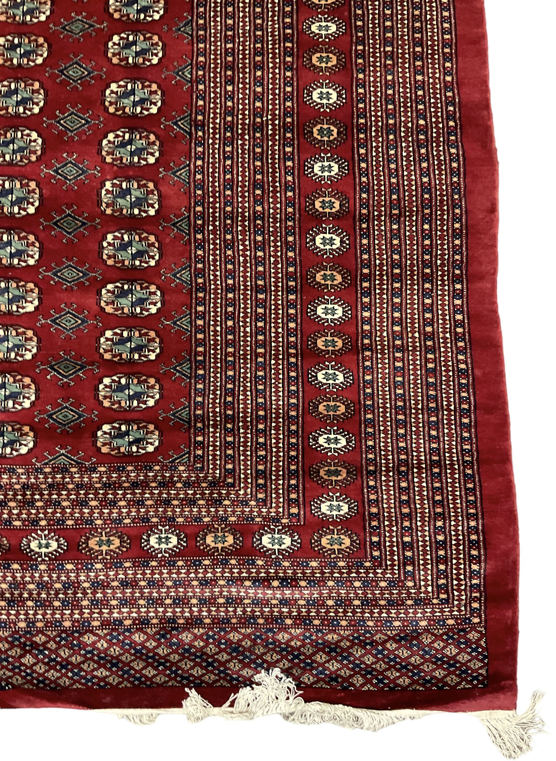 Large Persian Bokhara red ground carpet, the field decorated with eight rows of Gul motifs, wide multi-band borders decorated with repeating geometric motifs