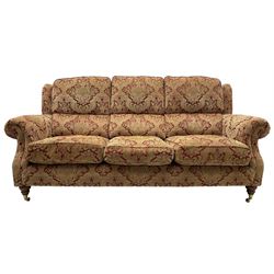 Parker Knoll - three-seat 'Oakham' hardwood-framed sofa, upholstered in red and gold floral pattern fabric, on turned feet with brass cups and castors 