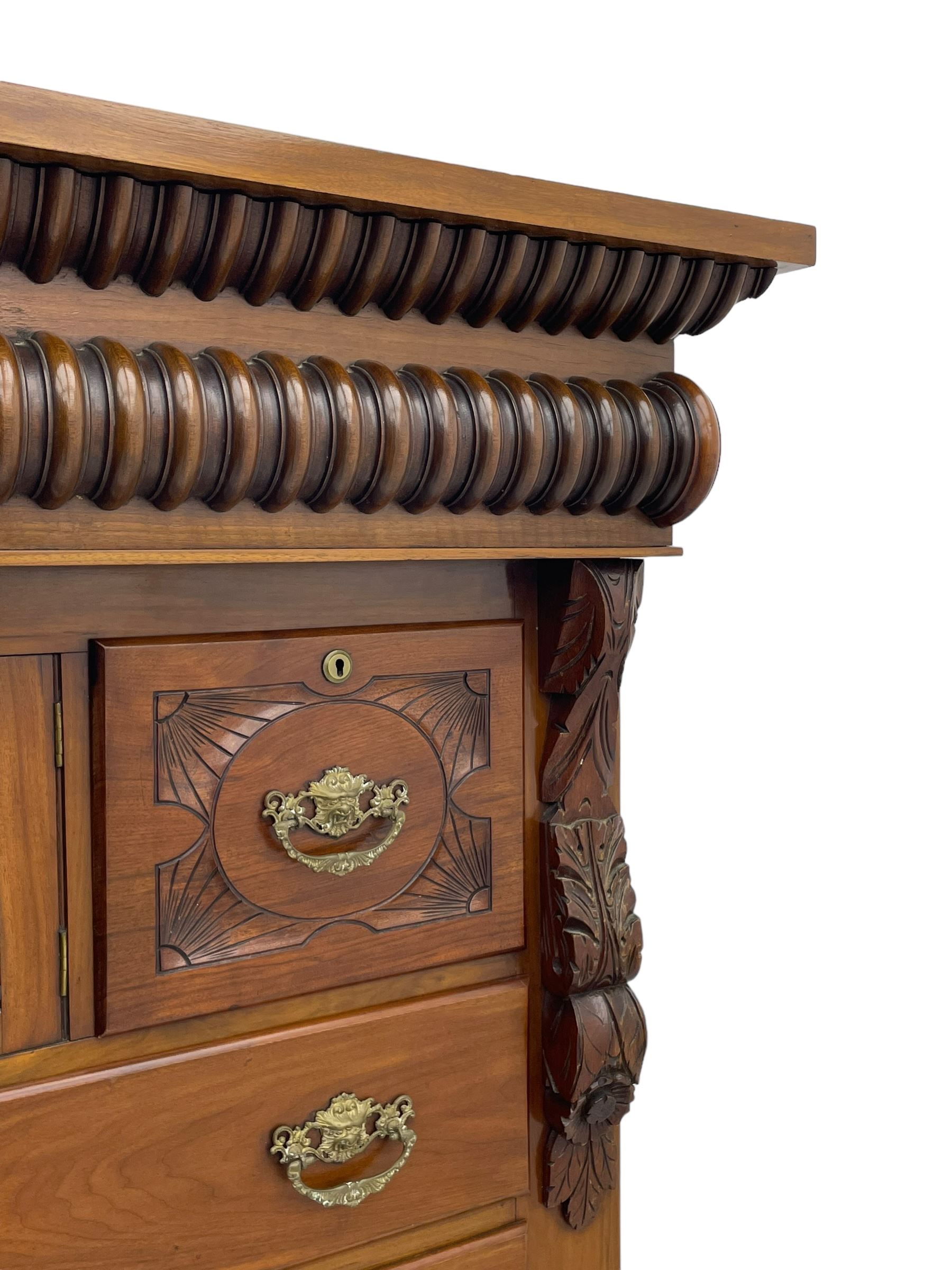 Late Victorian walnut Scotch chest, projecting cornice with turned quarter column mounts over matching half column to frieze, fitted with two upper short drawers with central cupboard, bevelled mirror glazed cupboard door, four graduating drawers below, foliage and flower head carved brackets to the uprights, panelled sides, chamfered plinth on turned feet