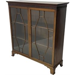 Early 20th century mahogany bookcase, projecting dentil cornice over blind fretwork frieze, enclosed by two astragal glazed doors, on shaped bracket feet 