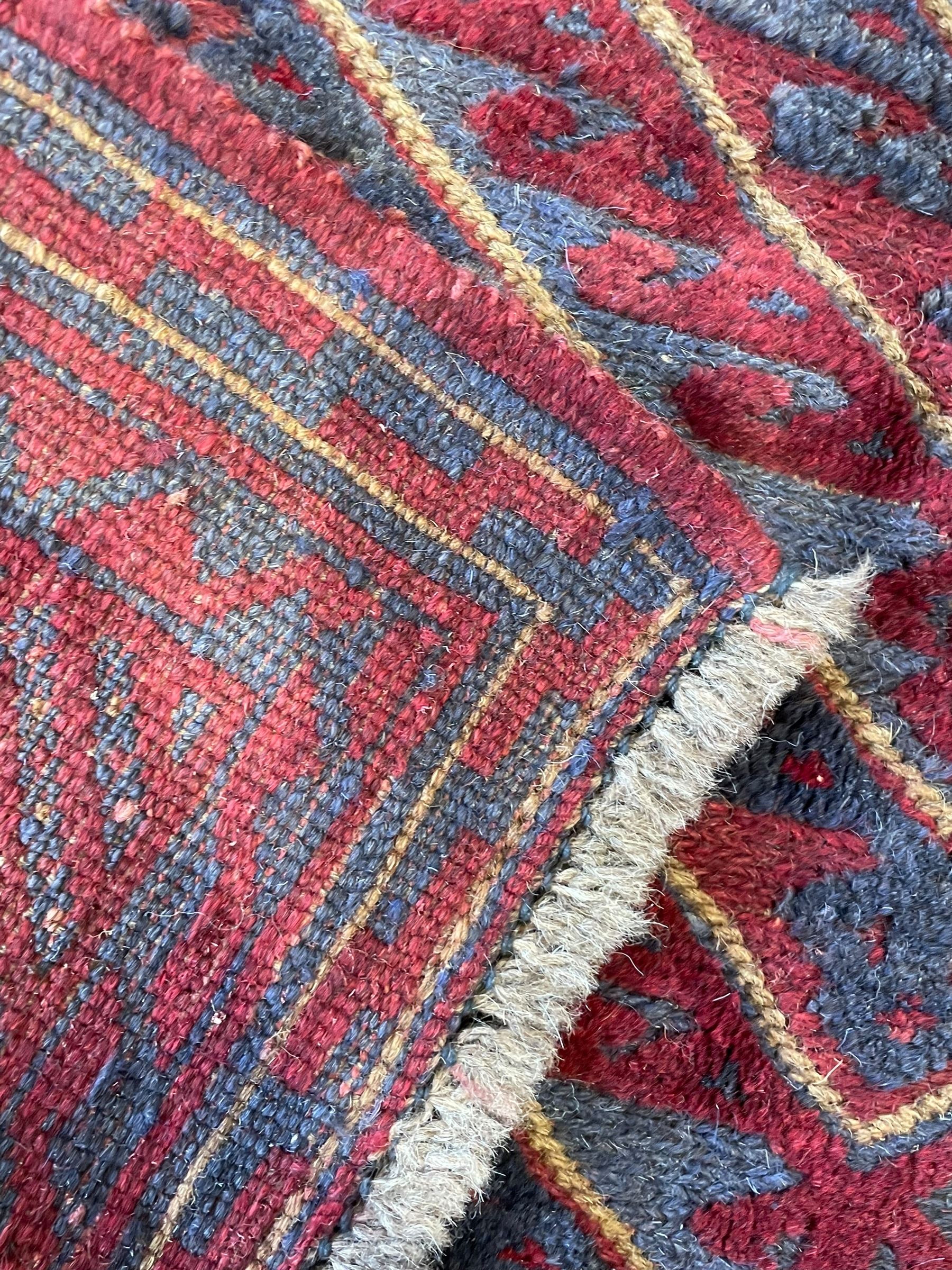 Meshwani indigo and maroon ground rug, the field decorated with a central lozenge with concentric borders containing hook motifs, enclosed by geometric zig-zag guard lines