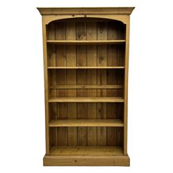 Pine open bookcase, projecting moulded cornice over arched frieze, fitted with four adjustable shelves, on plinth base