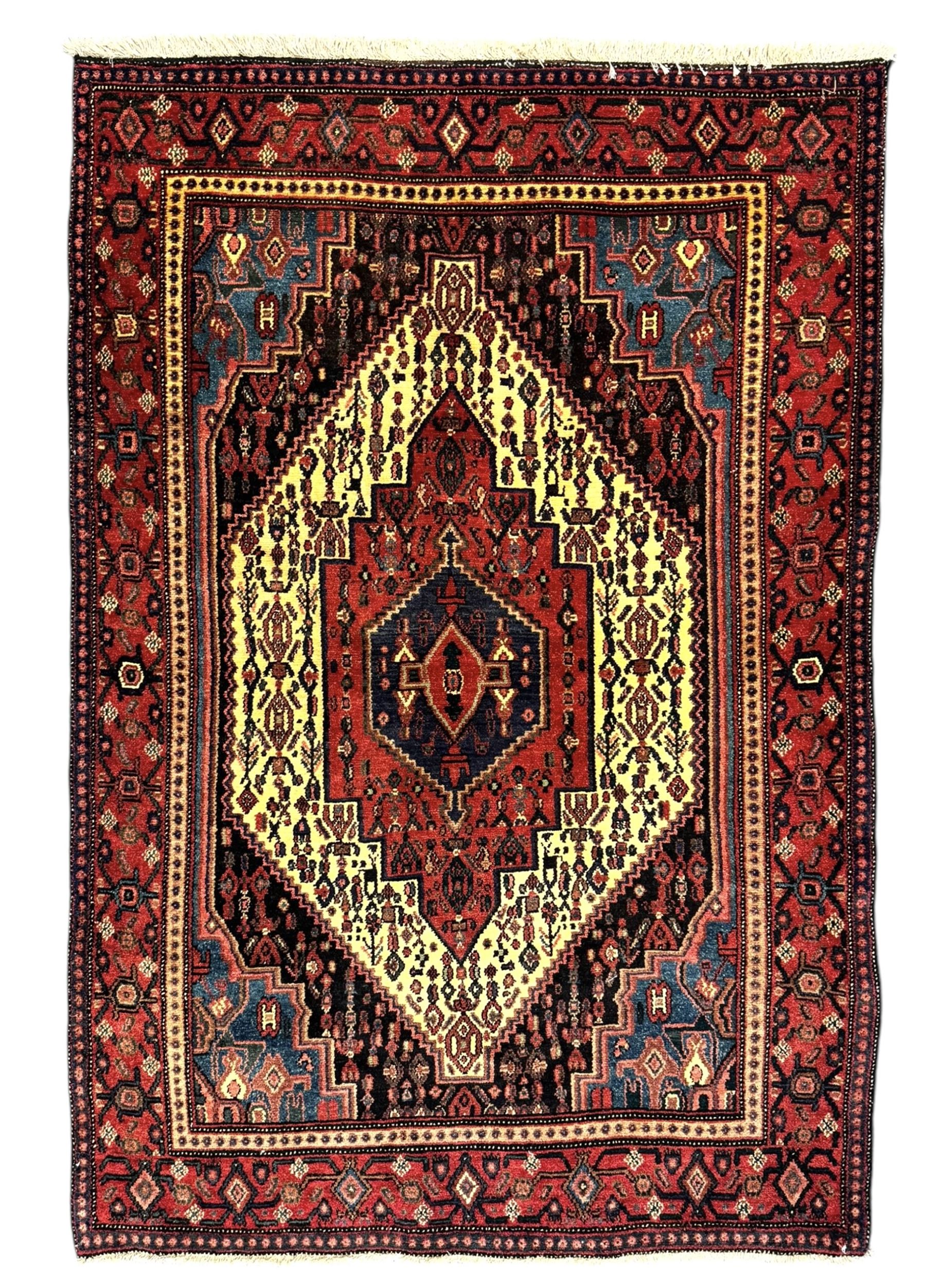 Northwest Persian Senneh crimson ground rug, central ivory lozenge medallion with geometric motifs, framed by matching spandrels, the surrounding field densely filled with stylised floral and foliate patterns, guarded border with repeating geometric and foliate motifs