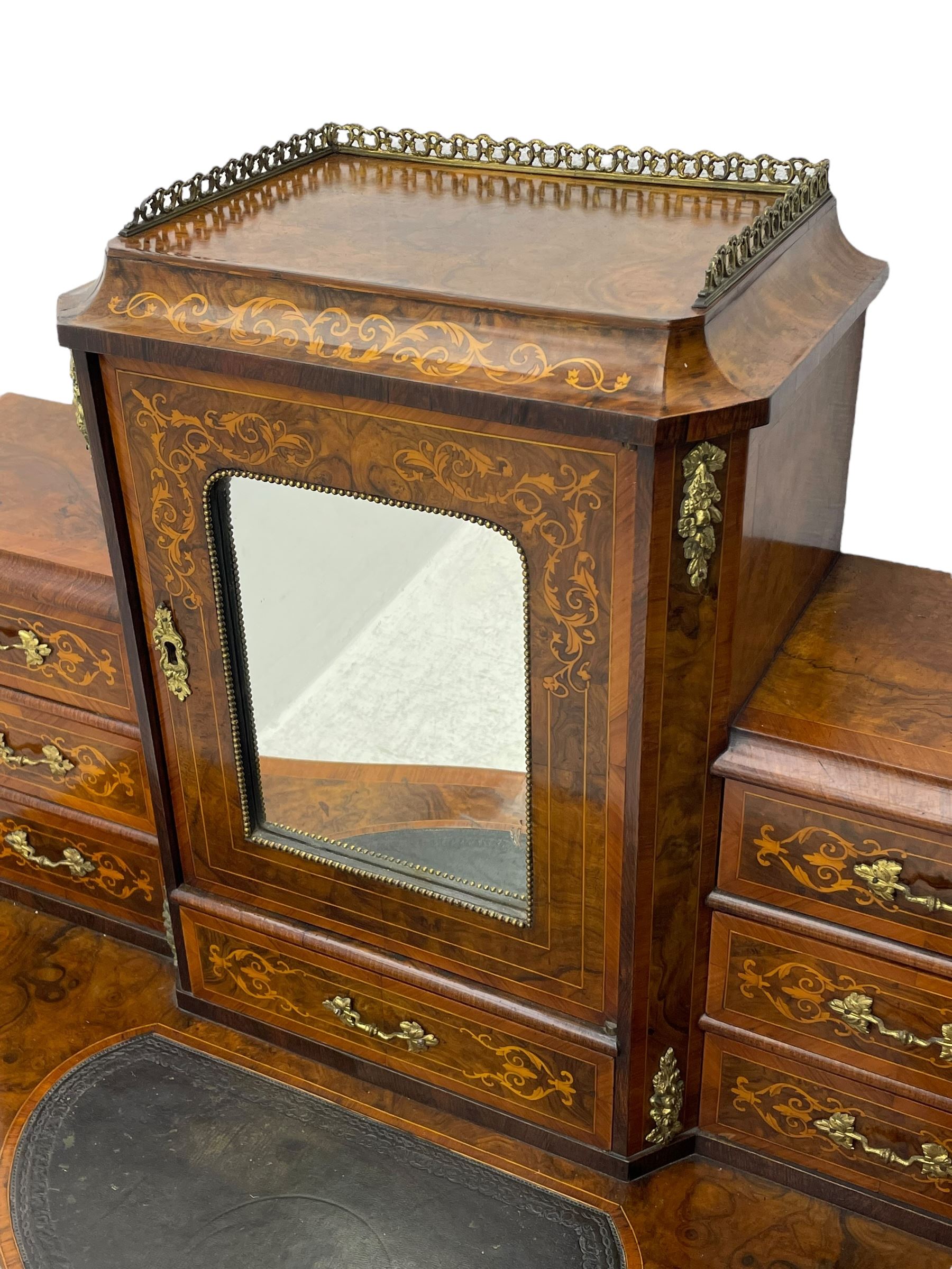 19th century French figured walnut Bonheur de Jour or writing desk, the upper section with brass gallery over mirror glazed cupboard and a combination of drawers, shaped and moulded top with leather inset and satinwood band, fitted with single drawer, on cabriole supports, inlaid throughout with scrolling foliate decoration in boxwood, ornate cast brass mounts 