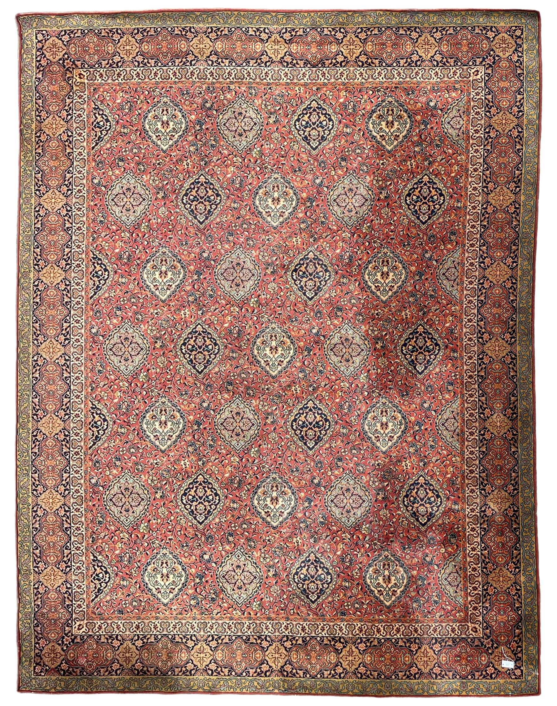 Large Persian design red ground carpet, the field decorated with multiple shaped panels surrounded by trailing leafy branches and stylised plant motifs, the guarded border decorated with shaped panels and floral pattern 