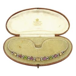 Early 20th century 15ct gold gold orange / yellow / peach topaz, pink tourmaline, pink sapphire peridot and diamond necklace, the pinks stones each set with four rose cut diamonds and spaced by scroll links with white enamel and black dots, to a trace link chain necklace, in fitted silk and velvet lined box by Skinner & Co