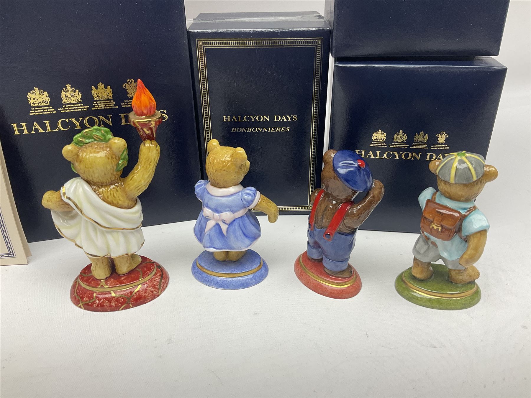 Eight Halcyon Days Teddy Bear of the Year figures, from 1993 to 2000, including one example modelled as a bear in Greek dress carrying a torch, one example modelled as a schoolboy and one example in a blue dress, all boxed 